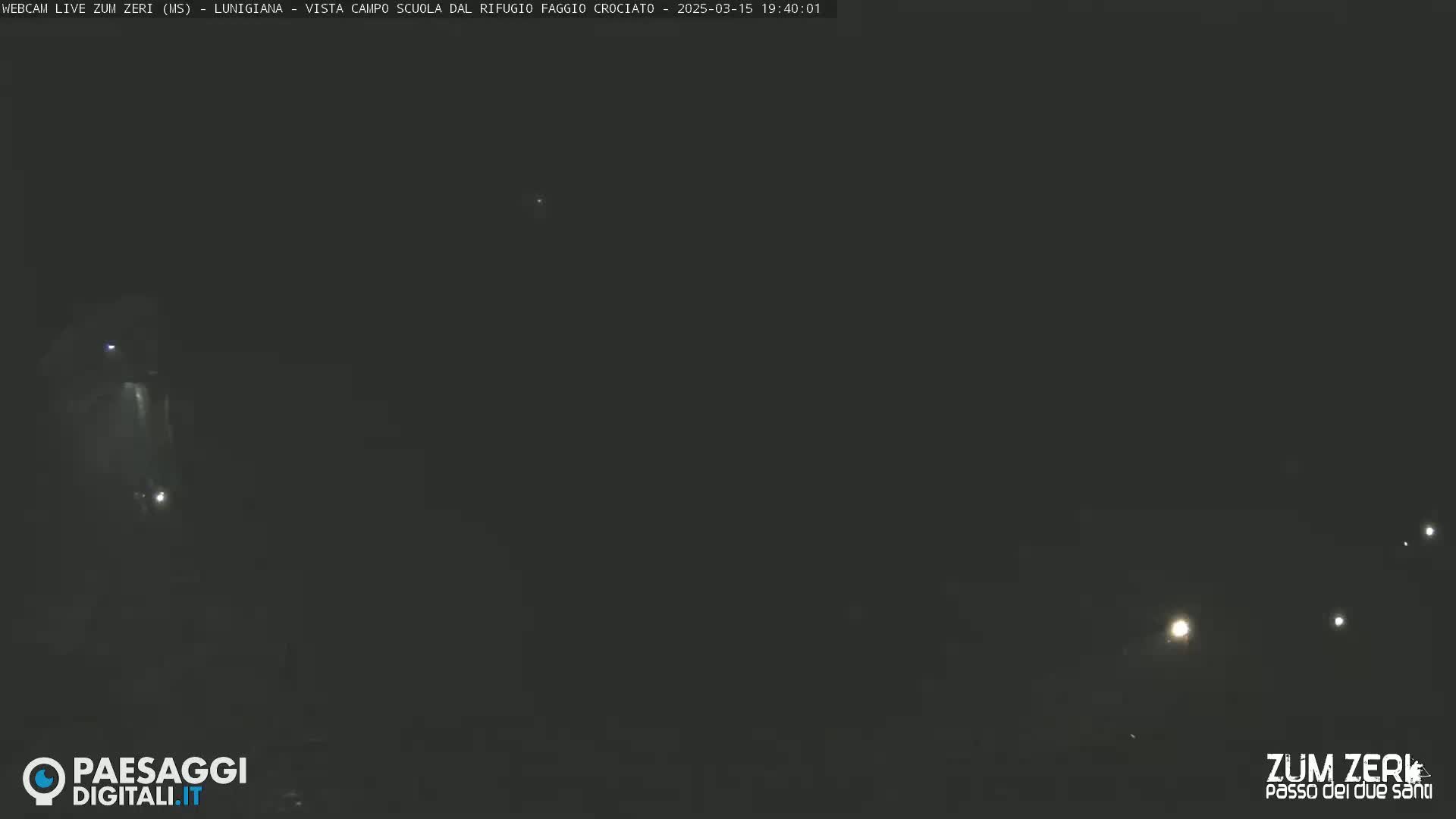 A nighttime, dark scene shows a few faint lights in the distance.