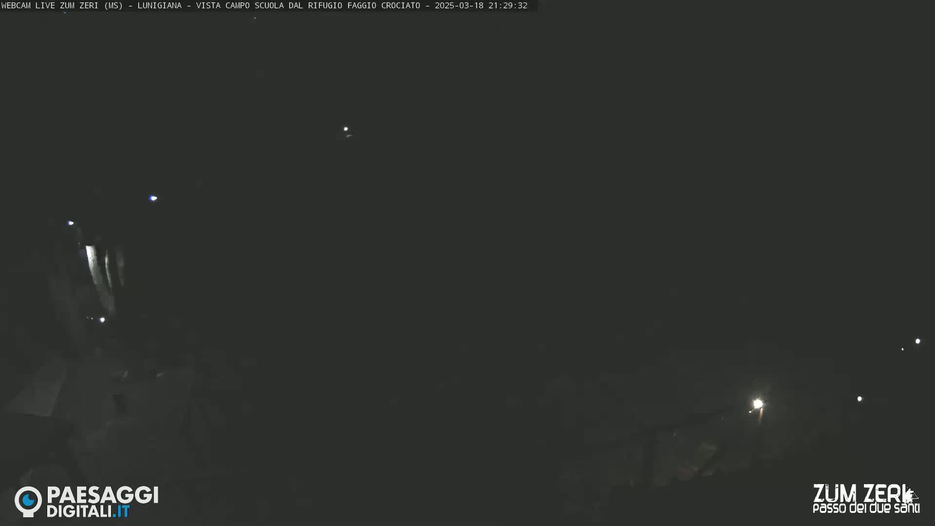 A dark, nighttime scene shows a few distant lights and a darker area in the foreground.
