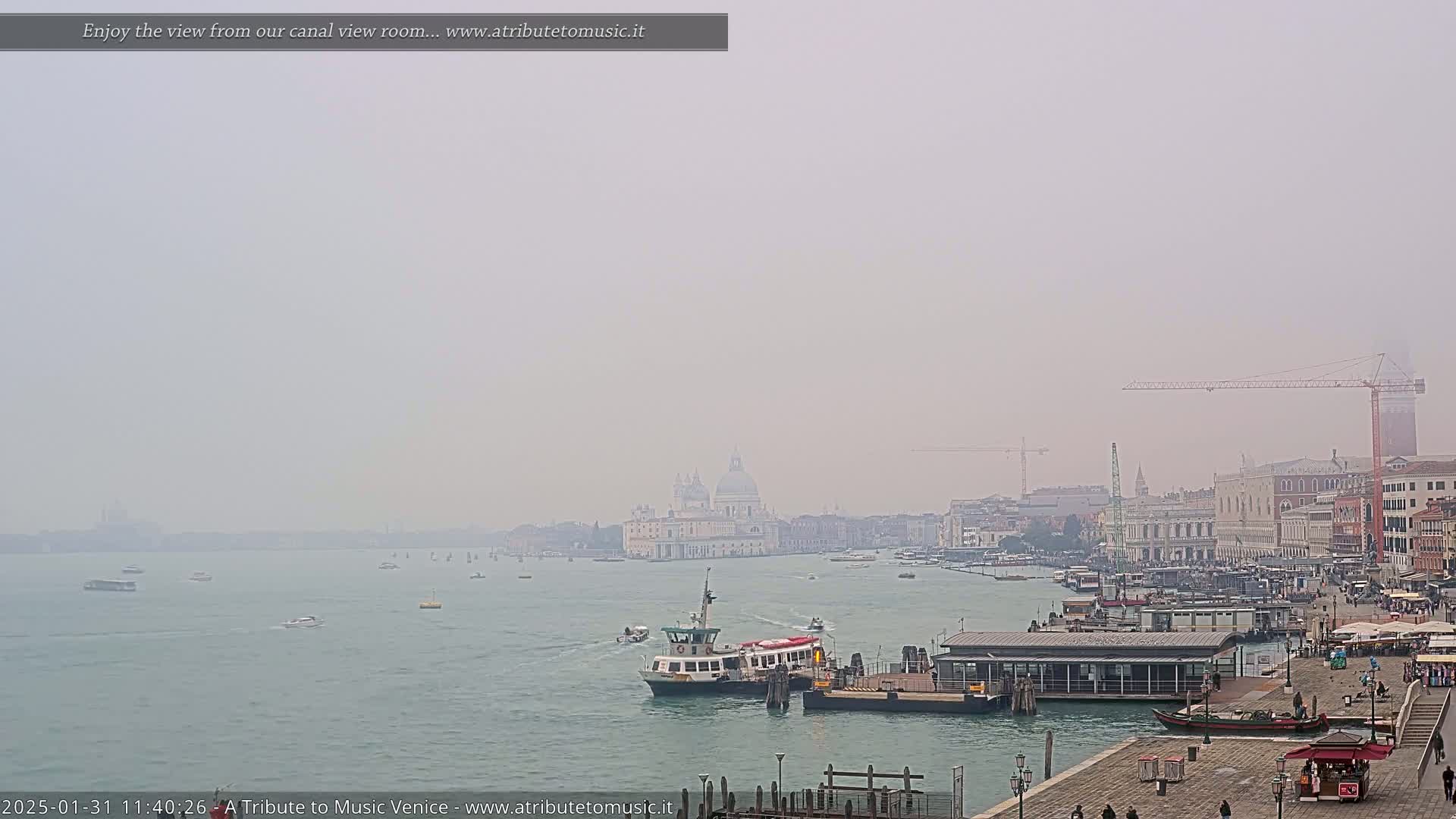 A hazy view of a Venetian canal shows a ferry boat near a dock, with buildings and a church visible in the distance.
