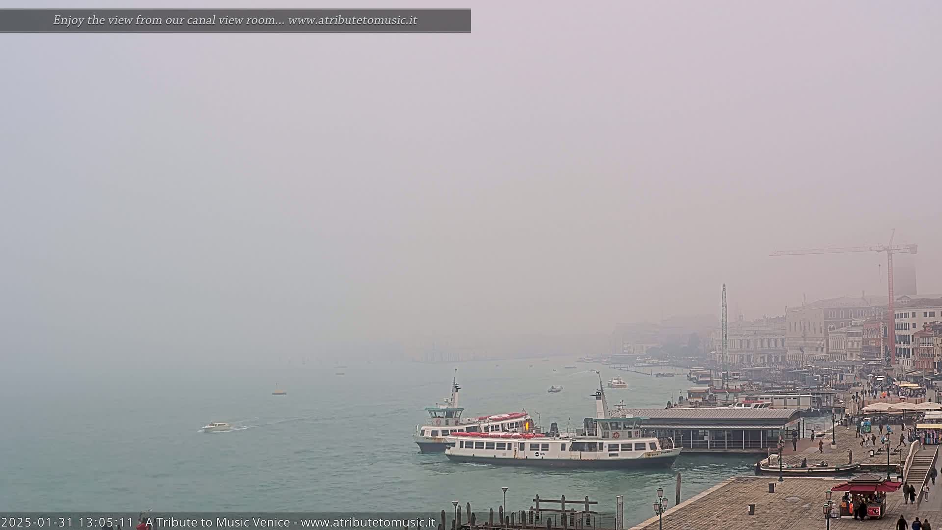 A foggy view of a canal in Venice, with several boats near a dock and buildings in the distance.