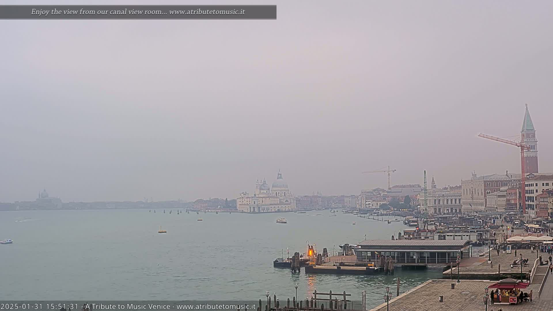 A hazy view of a canal in Venice, Italy, shows buildings, boats, and a construction crane.