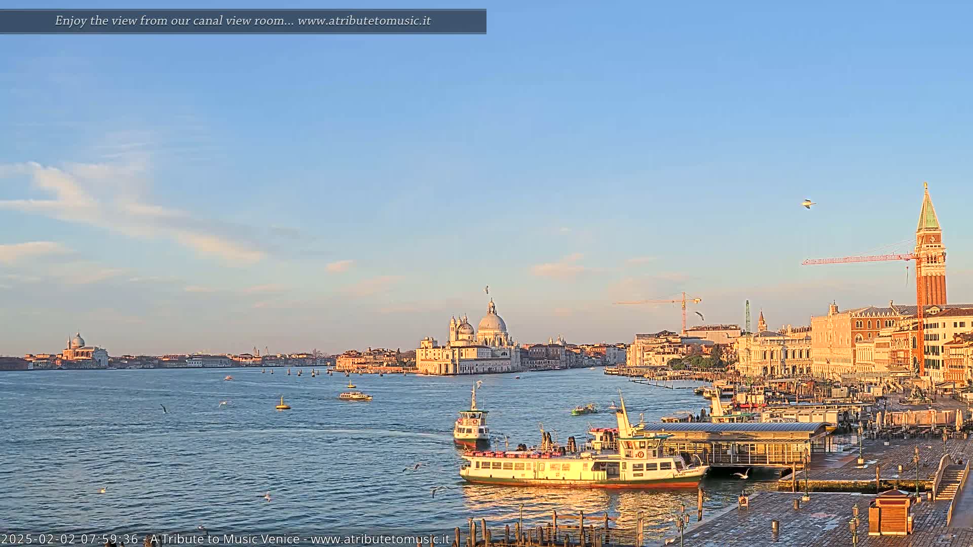 A sunny Venetian cityscape with calm water, several boats, and a large church is seen from a distance.