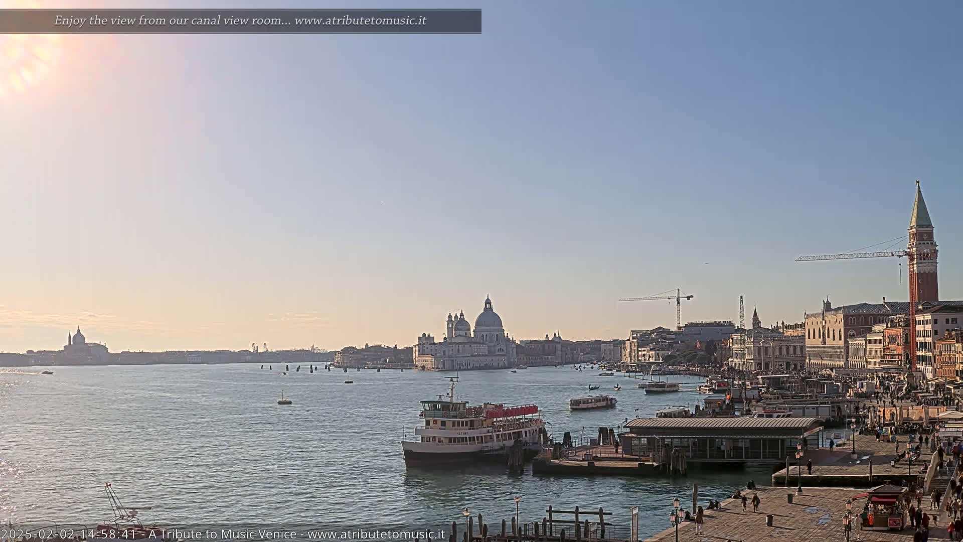 A sunny Venetian cityscape is visible across a calm canal, featuring a large church, several buildings, boats, and a tall bell tower.