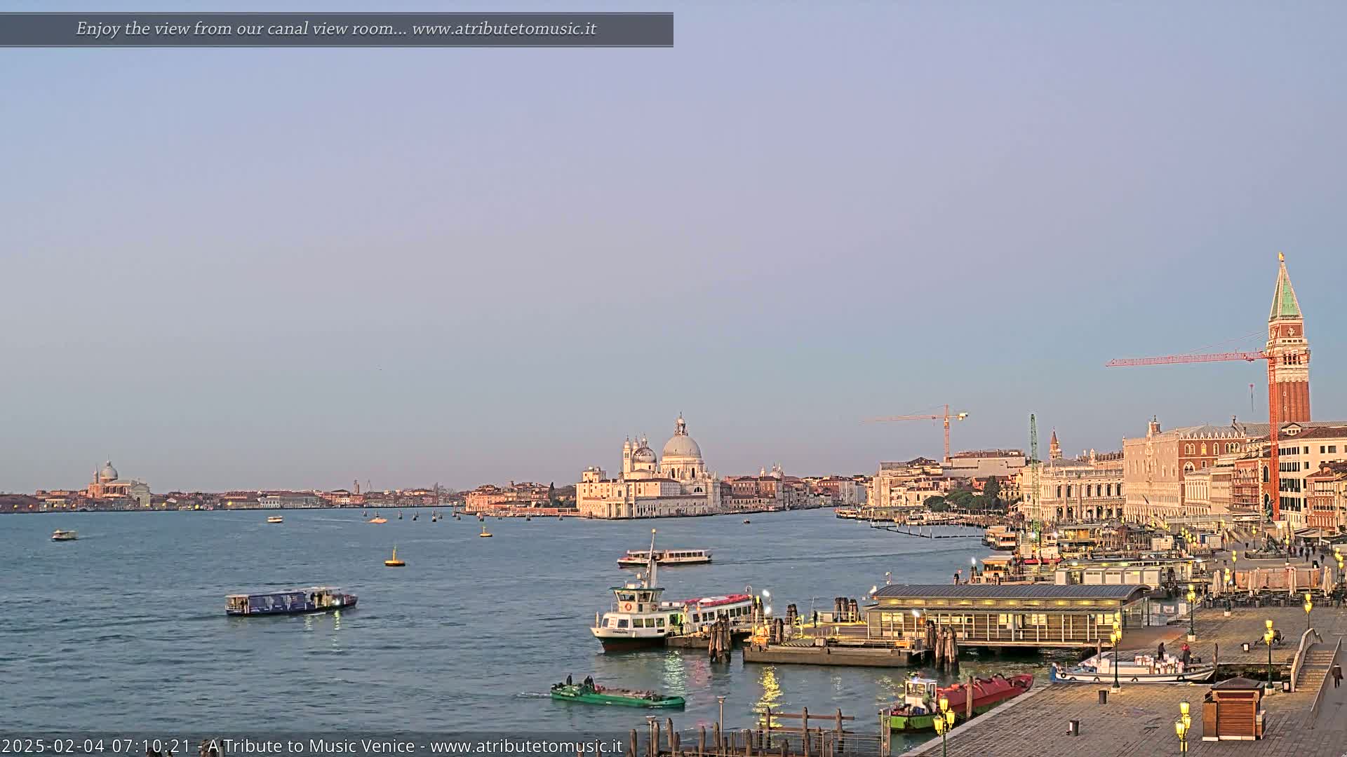 A tranquil Venetian canal scene at dawn, showcasing several water taxis and boats near a dock, with the Basilica di Santa Maria della Salute and St. Mark's Campanile visible in the distance.