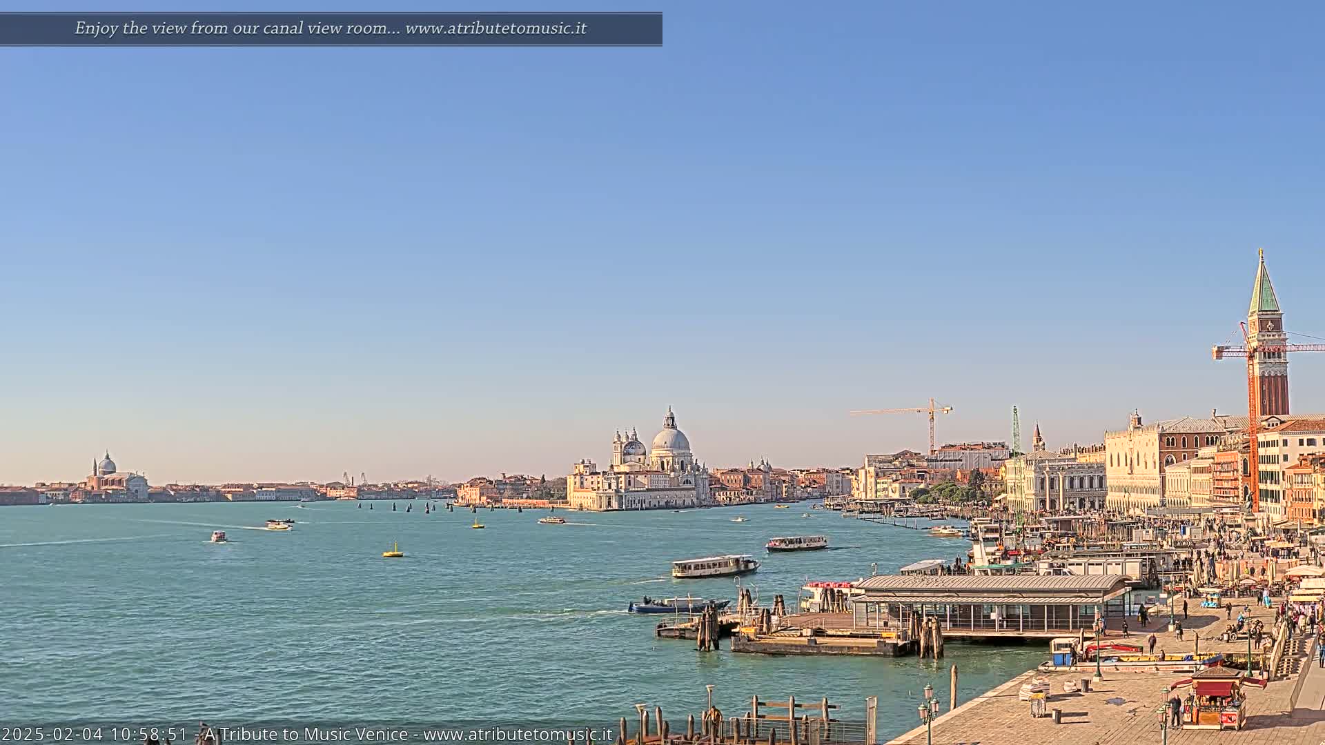 A wide shot of a Venetian canal shows numerous boats, a large church, and buildings lining the waterway under a clear blue sky.
