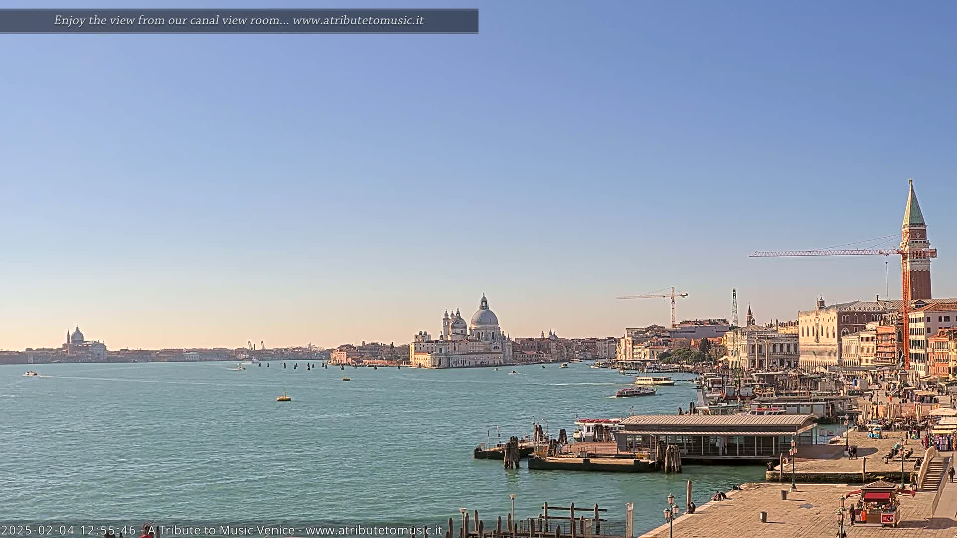 A wide shot of a Venetian canal on a clear, sunny day, showing the Basilica di Santa Maria della Salute and other buildings along the waterfront.