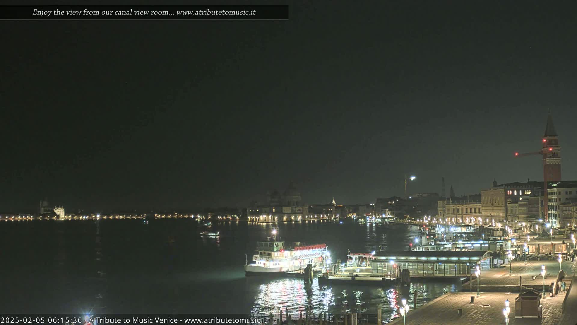 A nighttime view of a canal, featuring several boats and buildings along the waterfront, under a dark, clear sky.