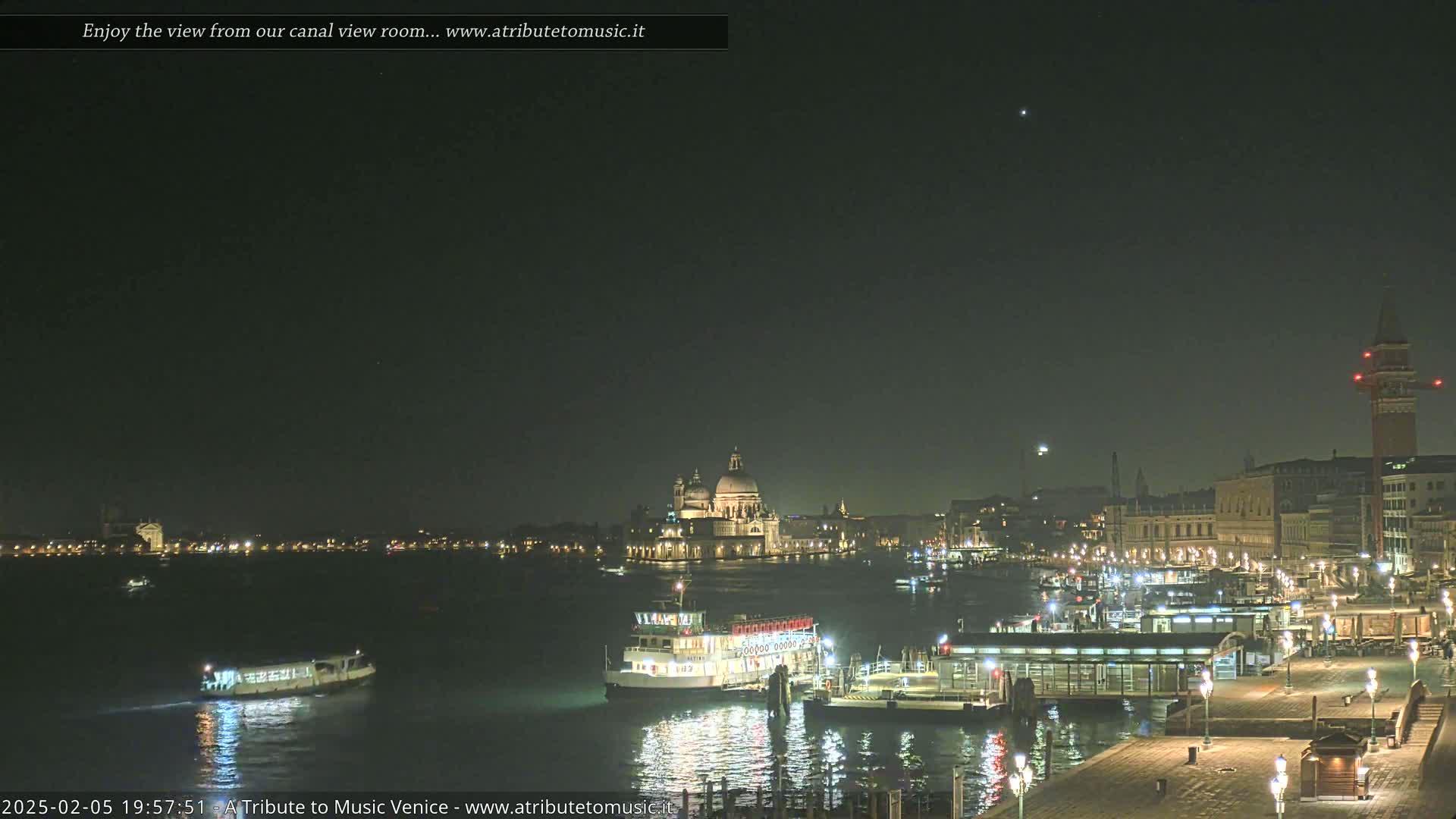 A nighttime view of a canal in Venice, showing boats, buildings, and a clear, dark sky.