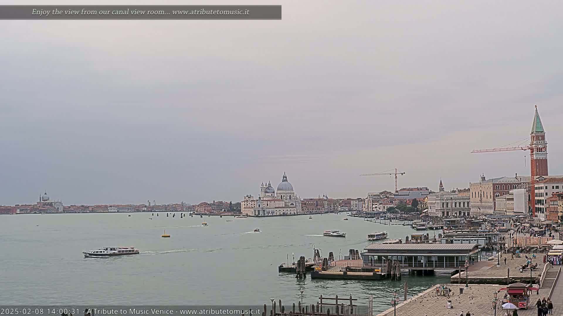 A wide shot of a Venetian canal shows boats on the water, buildings lining the shore, and a cloudy sky.