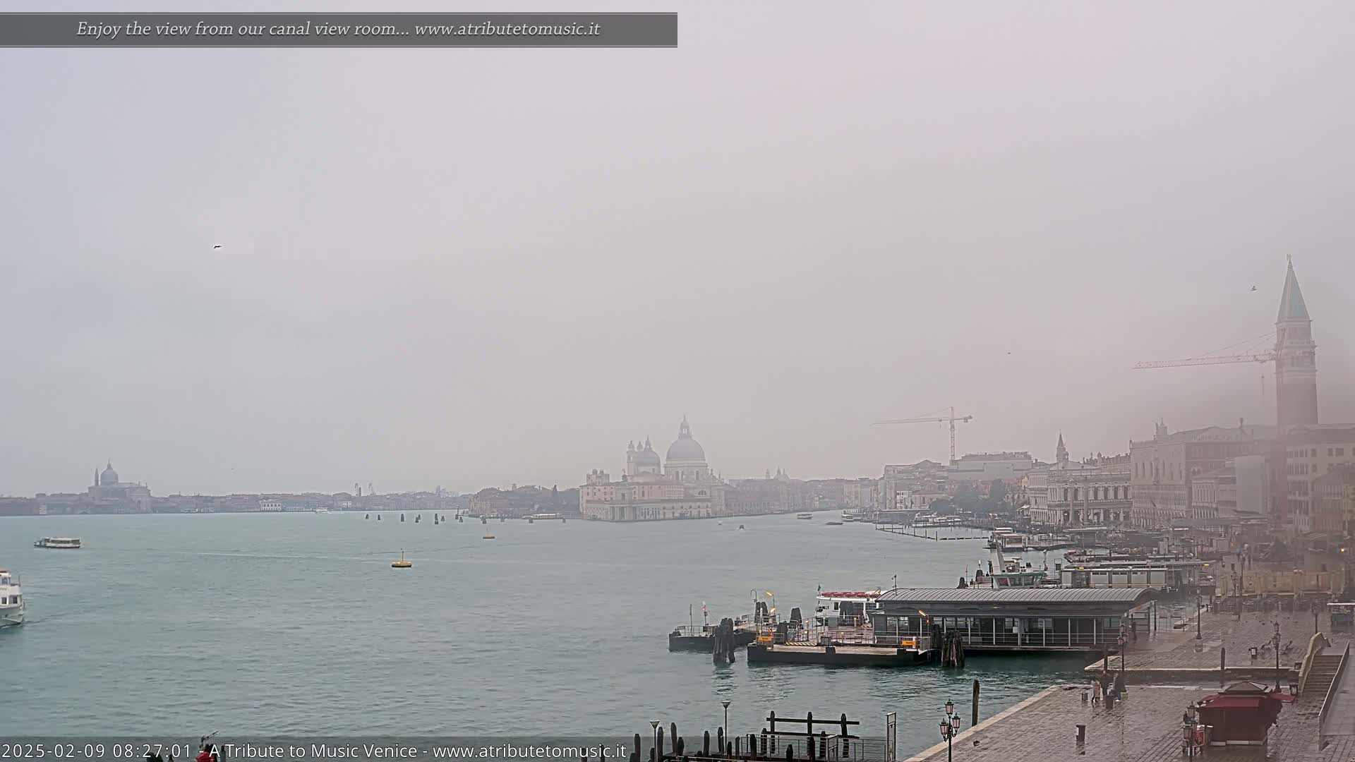 A foggy view of a Venetian canal with boats, buildings, and a church dome in the distance.
