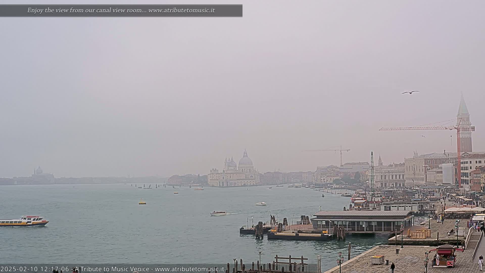 A hazy, overcast view shows a waterway with boats and a distant cityscape including a large domed building.