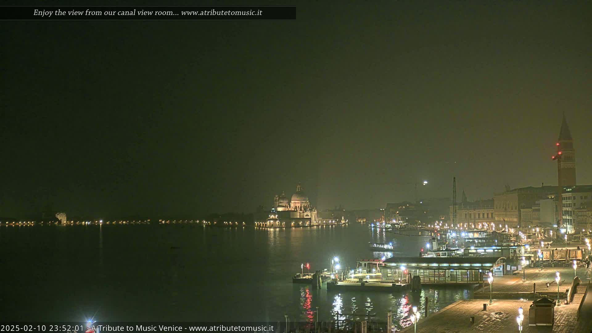 A hazy night scene shows a canal with boats and buildings, including a large domed structure and a tall bell tower, illuminated under dim ambient light.