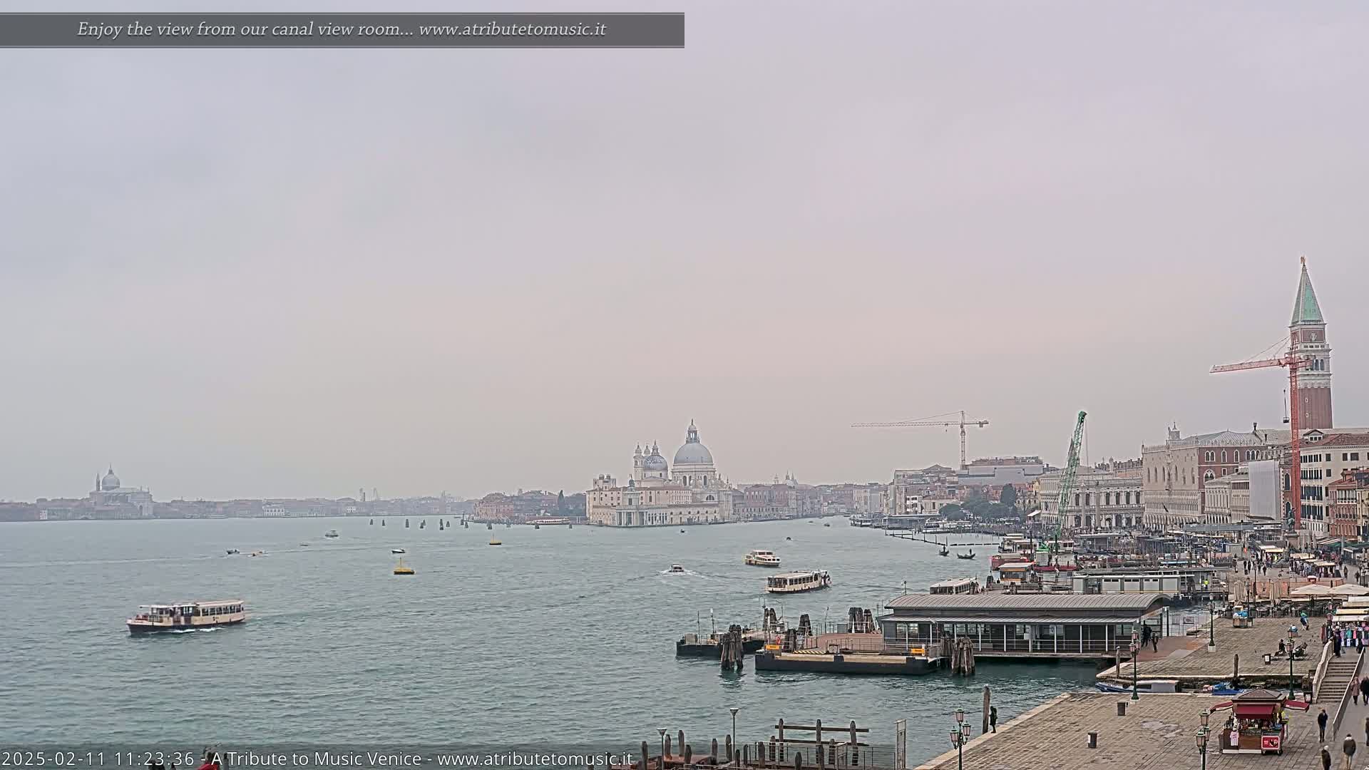 A hazy view of a Venetian canal shows boats, buildings, and a large church in the distance.