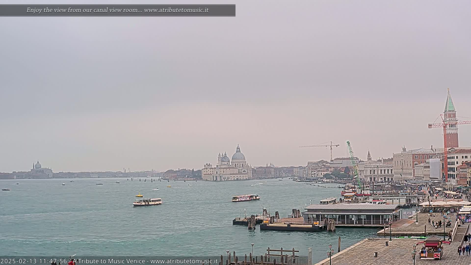 A hazy view of a Venetian canal, showing boats, buildings, and a large church, under an overcast sky.