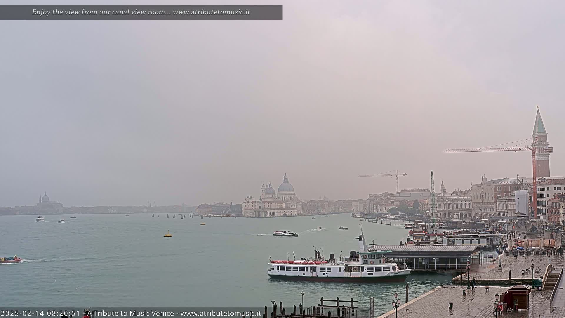A hazy, overcast day reveals a view of Venice's canal, with boats and buildings, including a large church, visible in the distance.