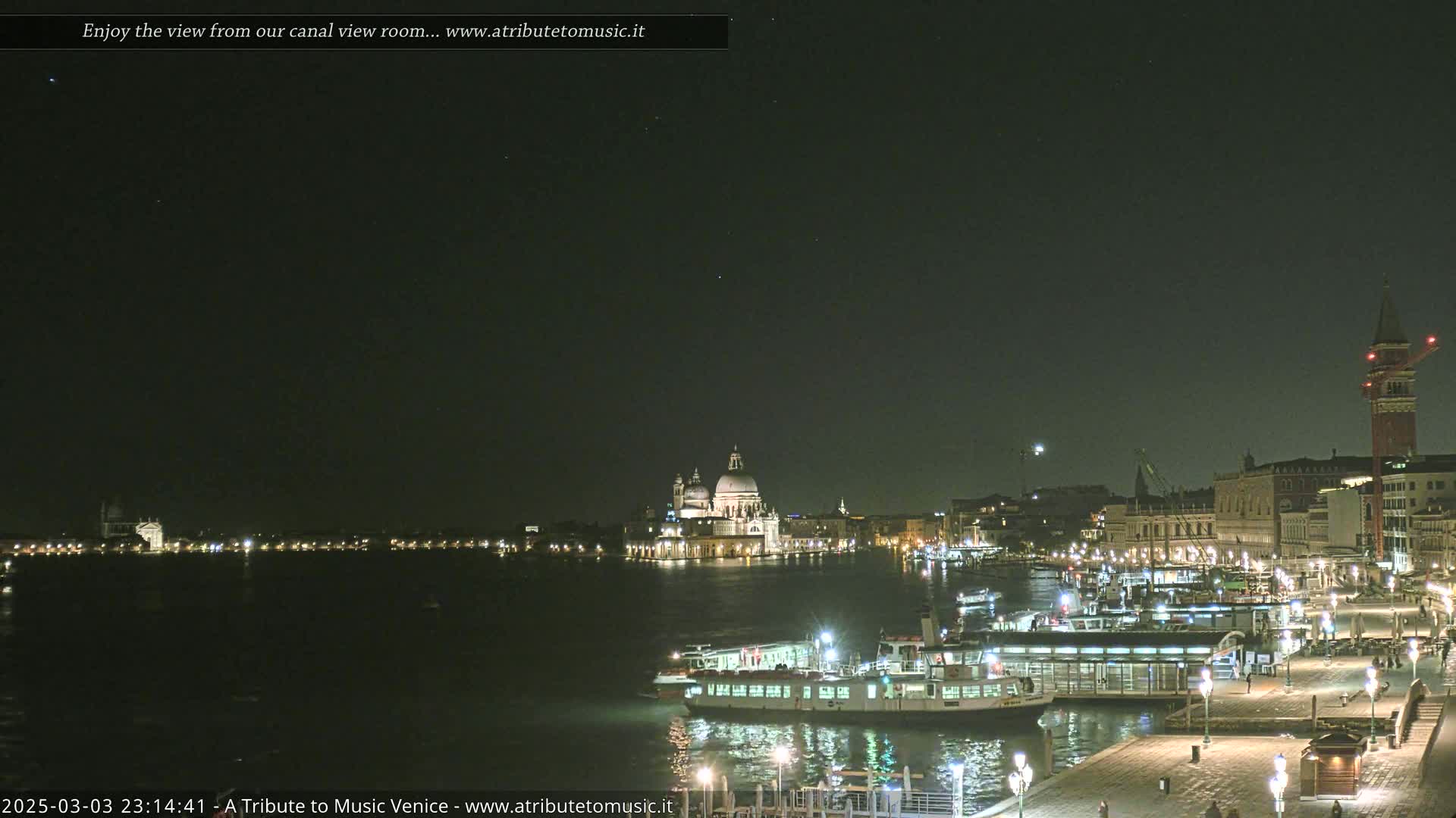 A nighttime view of a canal in Venice, showing illuminated buildings, boats, and a clear, starlit sky.