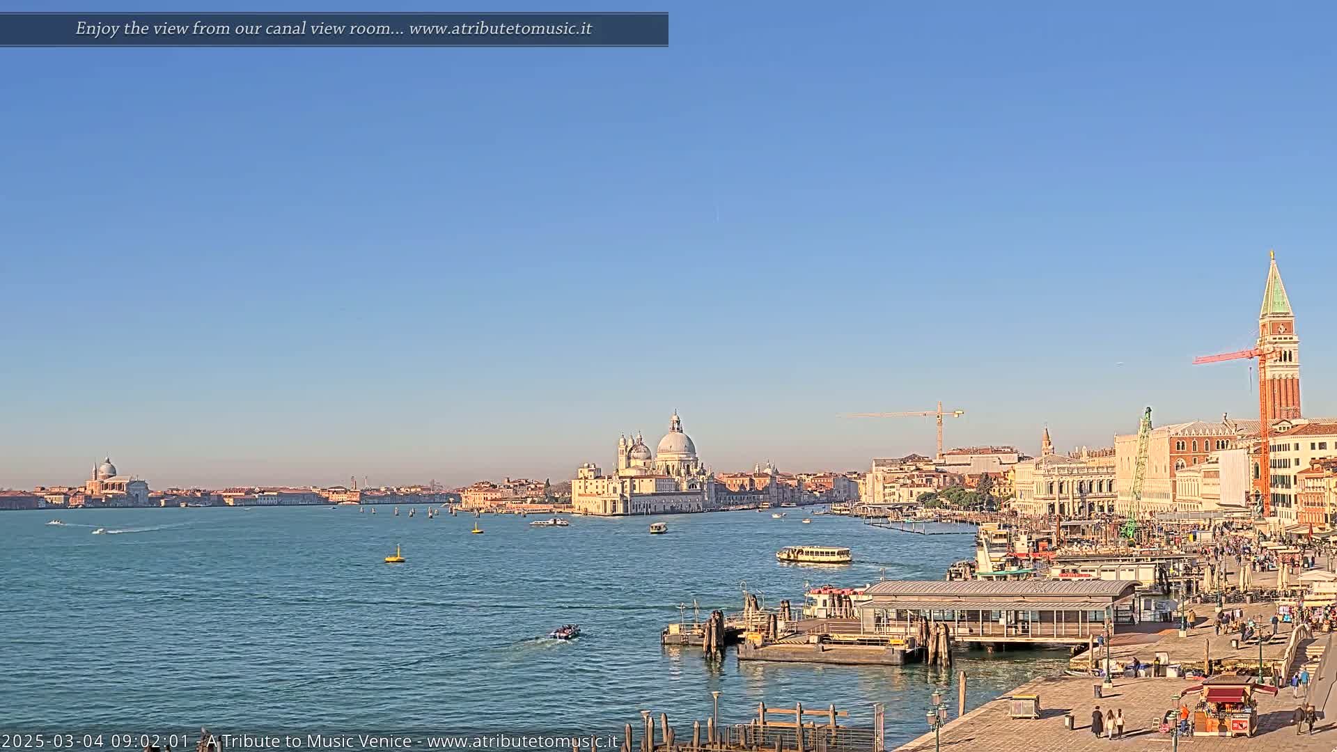 A sunny day reveals a Venetian cityscape across a calm canal, with boats and a large building prominently featured.