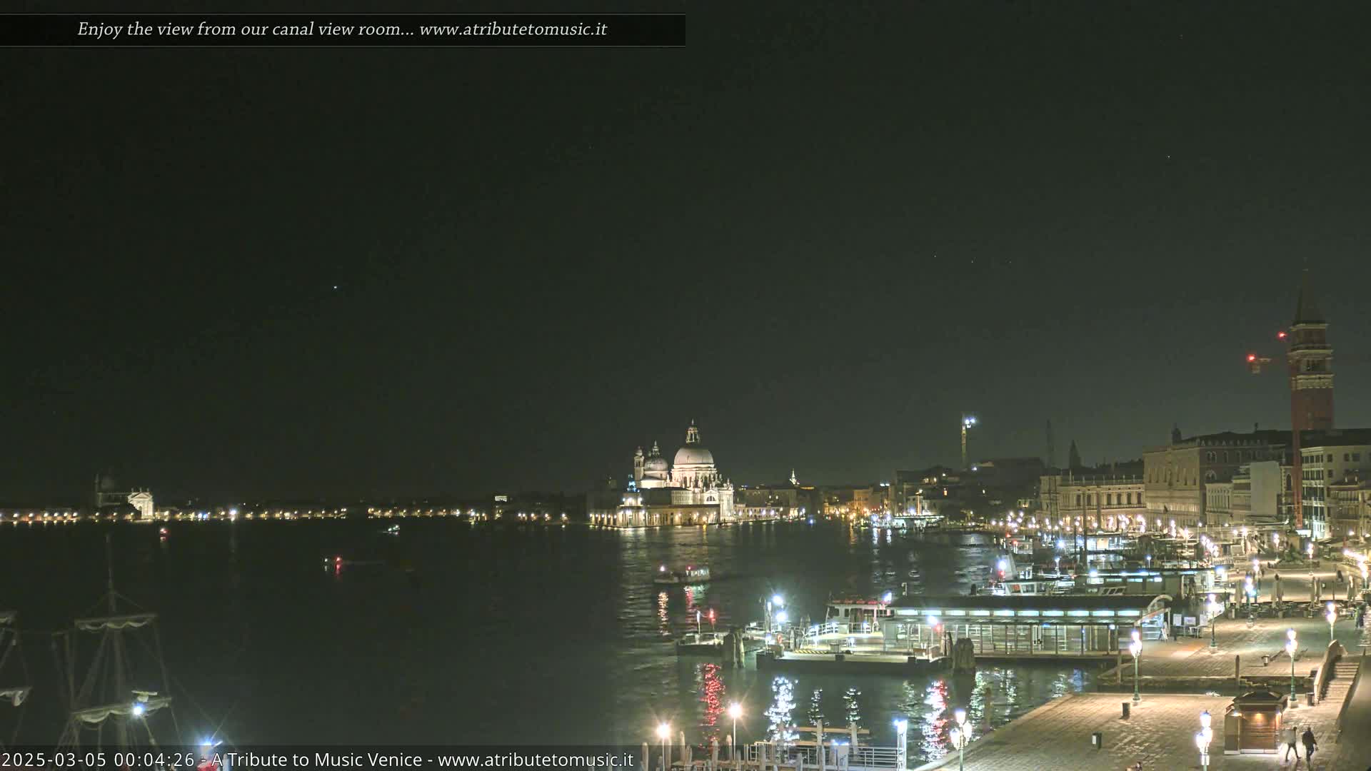 A nighttime view of a canal in Venice, showing illuminated buildings and boats under a clear, dark sky.