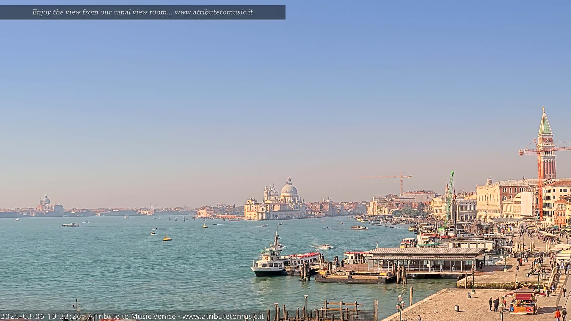 A clear, sunny day reveals a Venetian waterway with boats, a waterfront cityscape, and a prominent church dome in the distance.