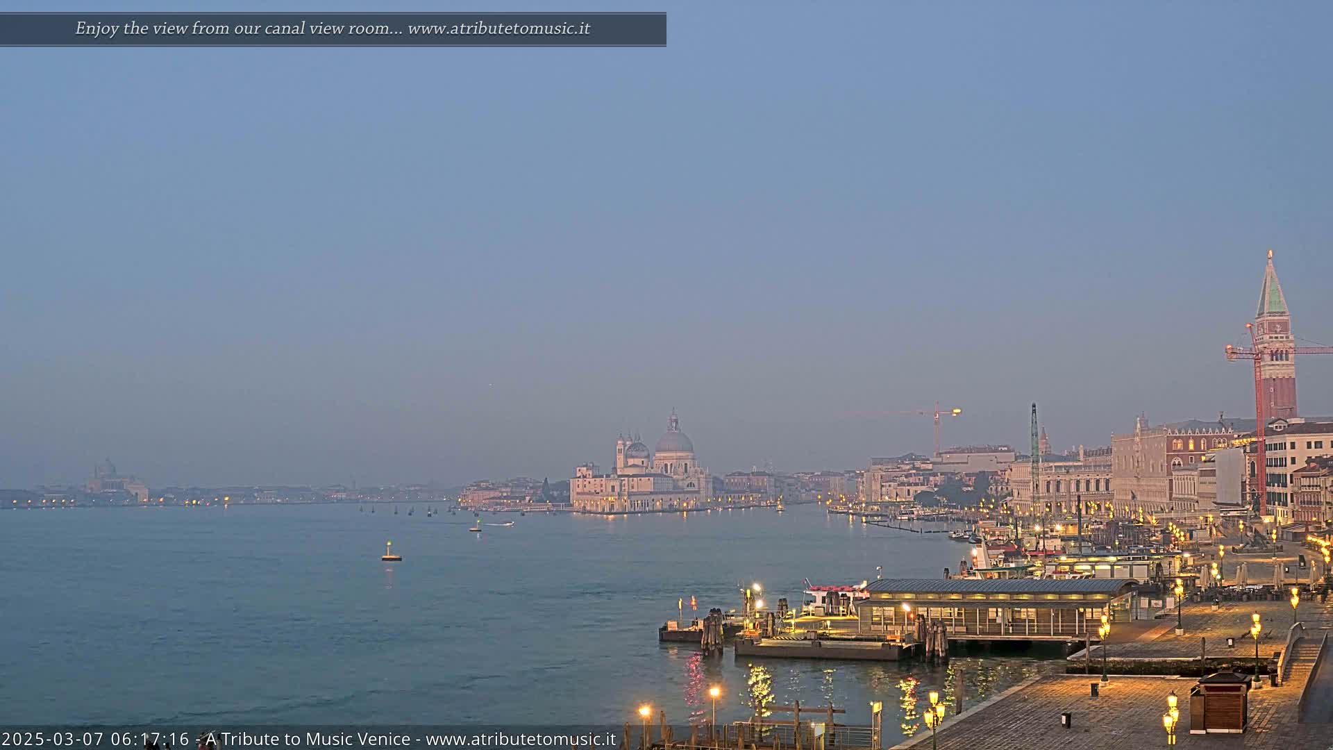 A hazy twilight view across a calm Venetian canal, showing a city skyline with a large domed church and a tall bell tower.