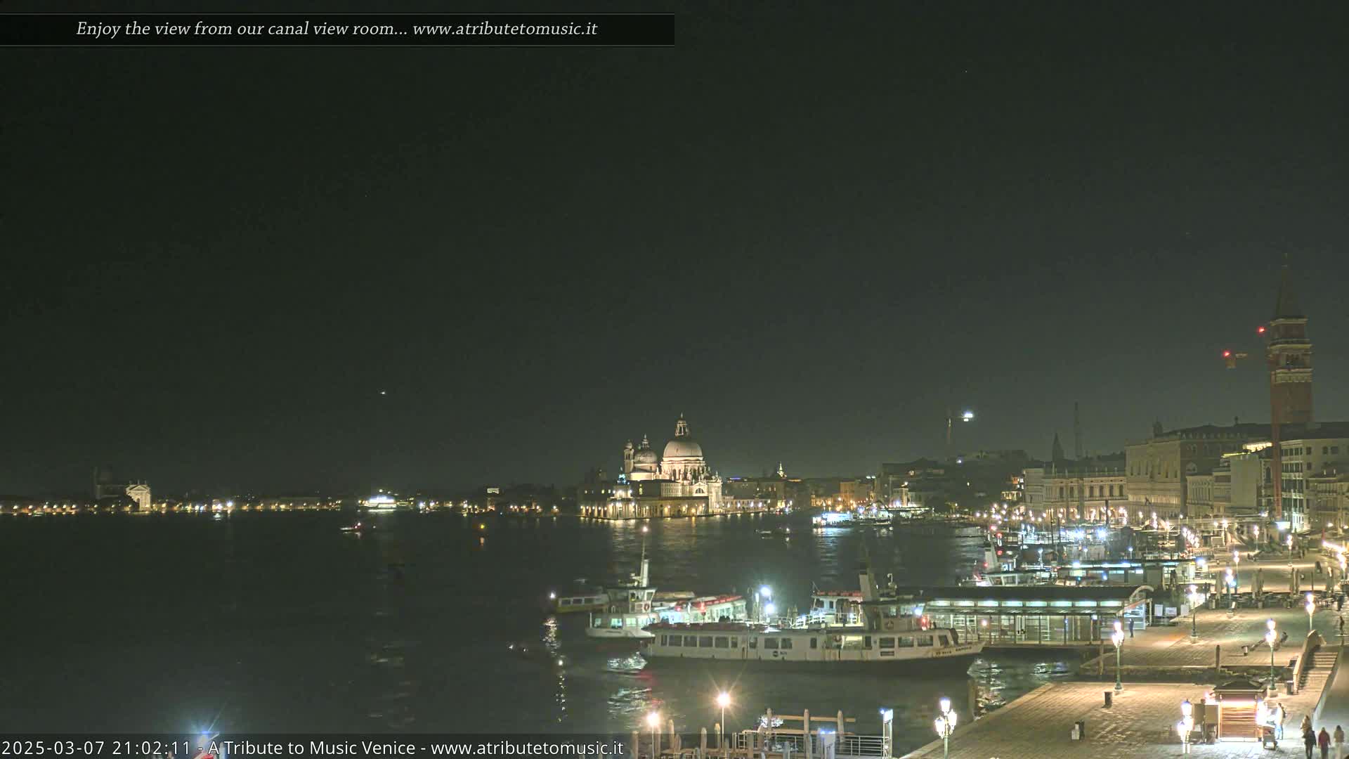 A nighttime view of a canal in Venice, with illuminated buildings and boats, under a dark sky.
