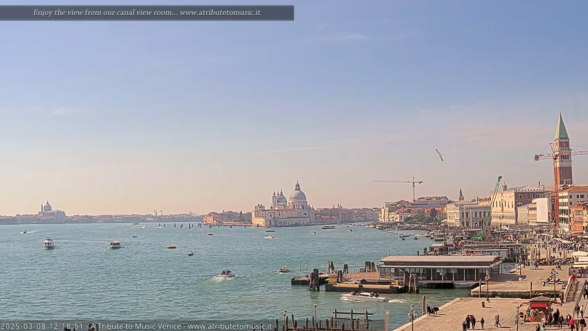 A sunny view of a Venetian canal with boats, buildings, and a large church in the distance.