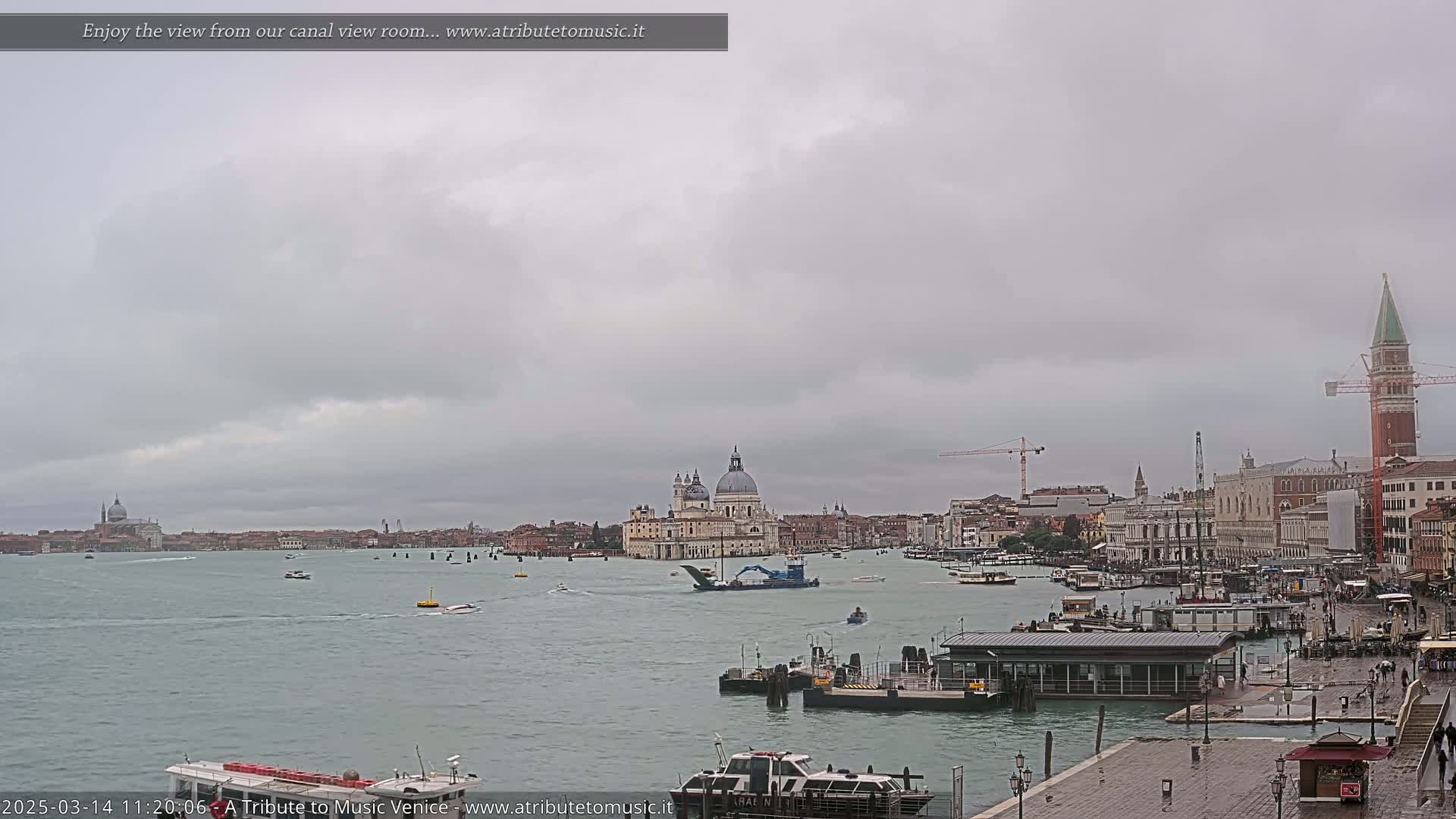 A wide shot of a waterway in Venice, Italy, shows several boats and buildings on a cloudy day.