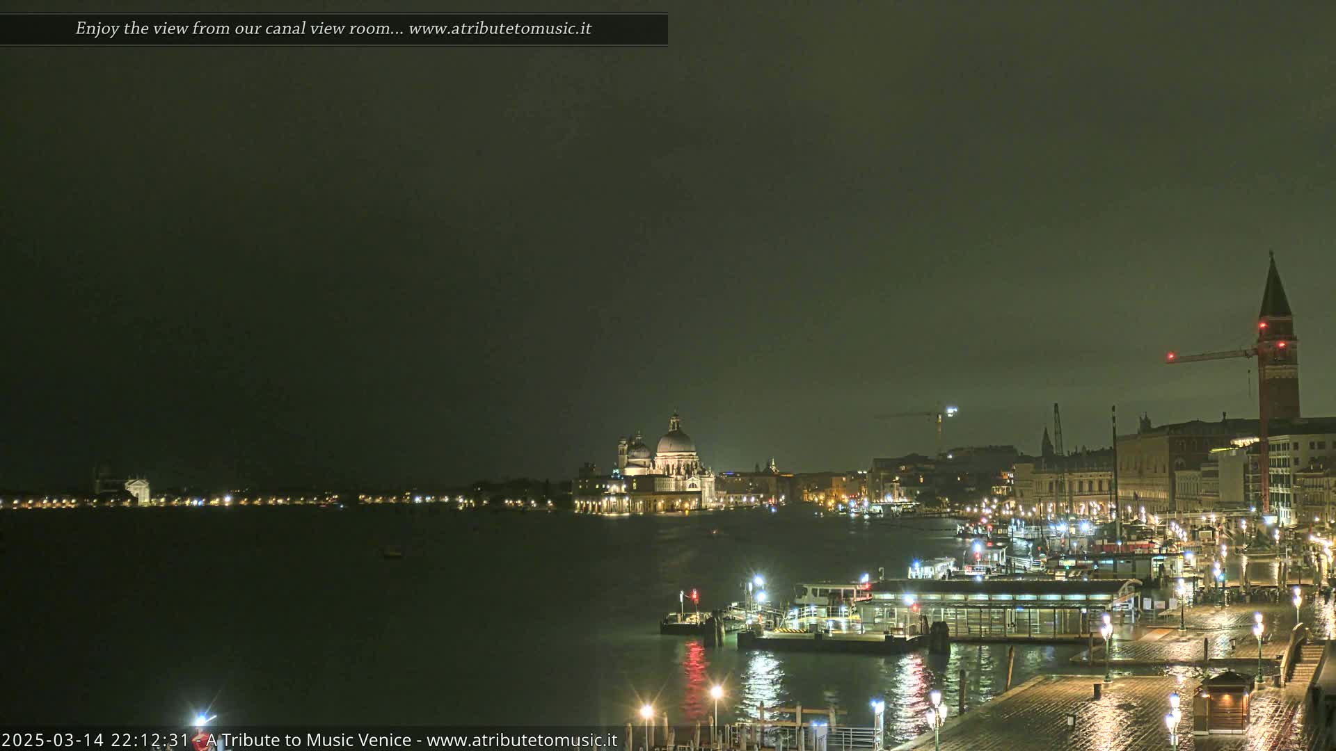 A nighttime view of a canal in Venice, showing illuminated buildings and boats under a dark, overcast sky.