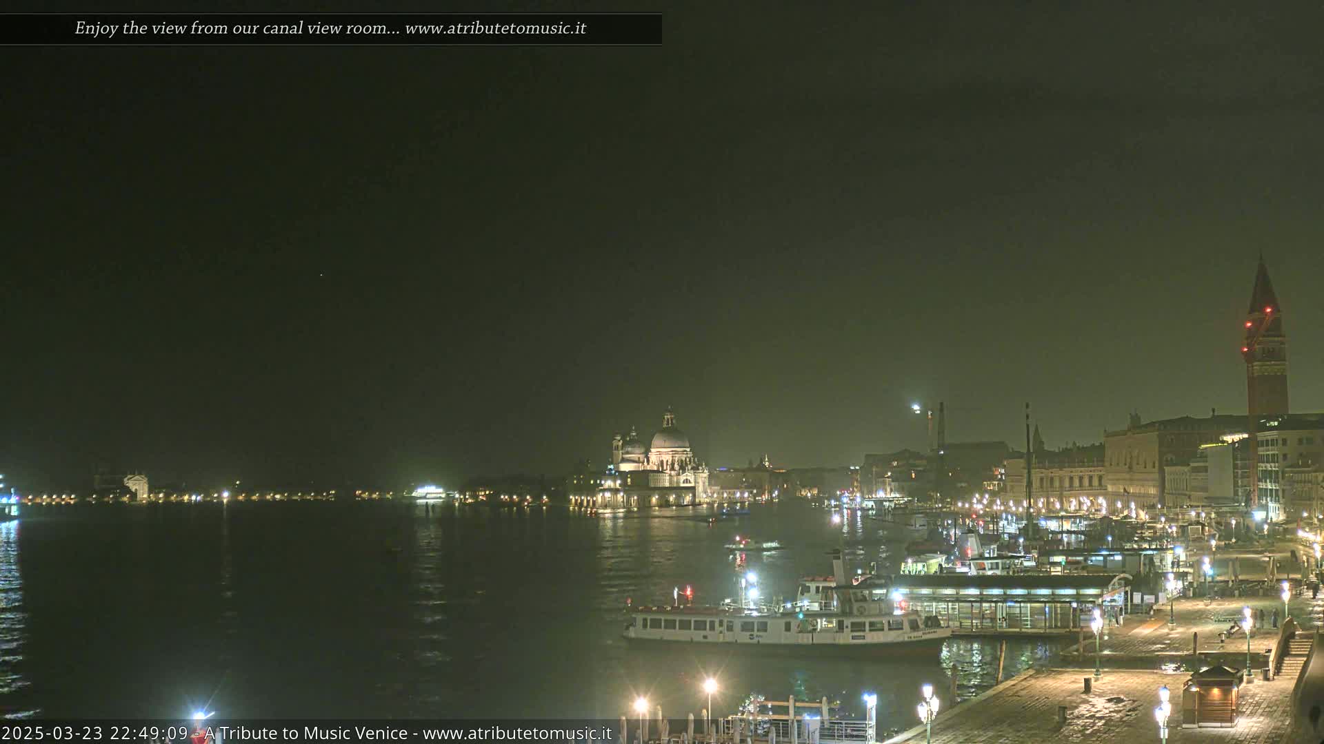 A nighttime view of a canal in Venice, showing illuminated buildings, boats, and a church, under a dark sky.