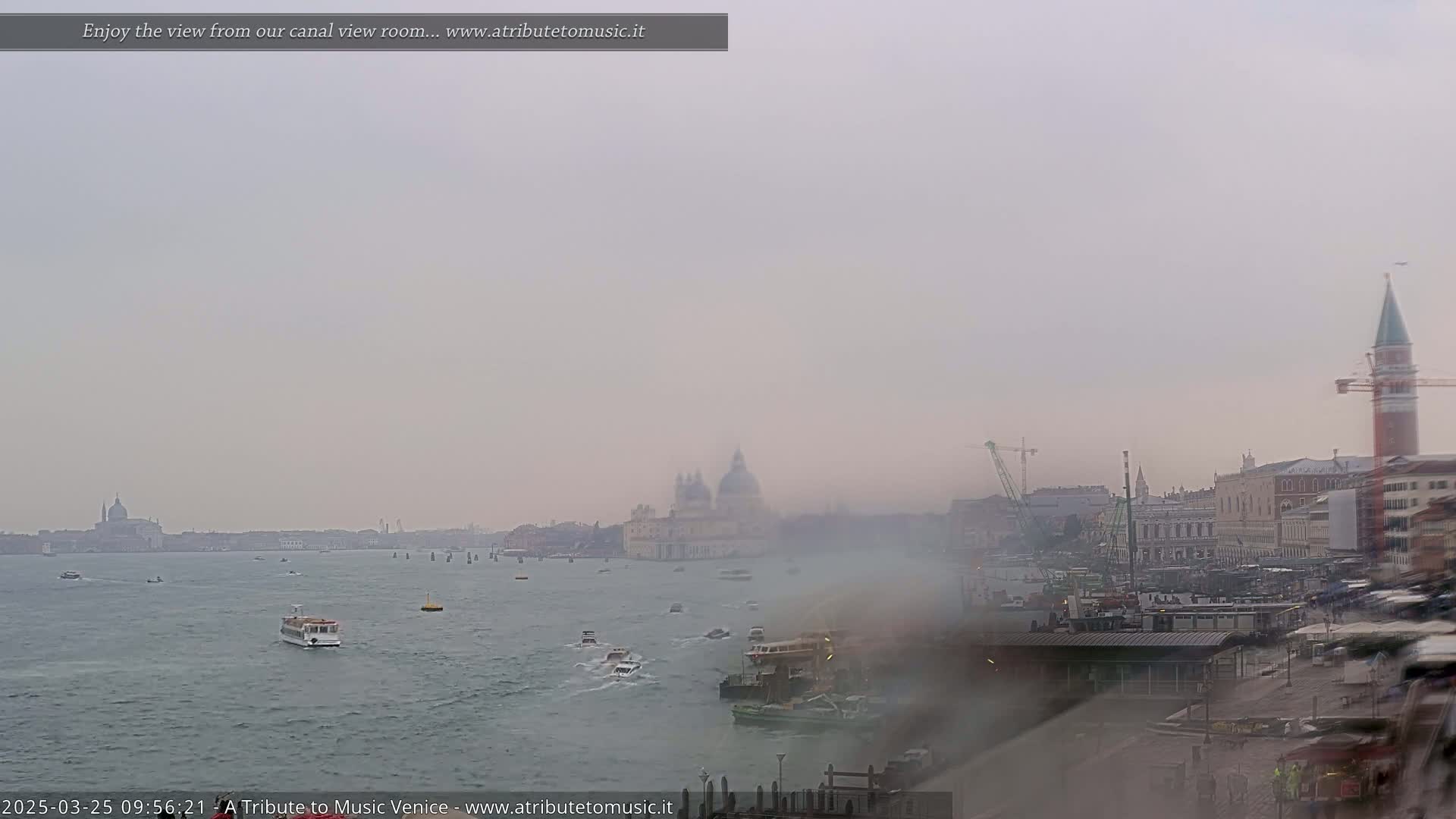 A hazy view of a canal in Venice, with boats on the water and buildings along the shoreline, under a muted sky.