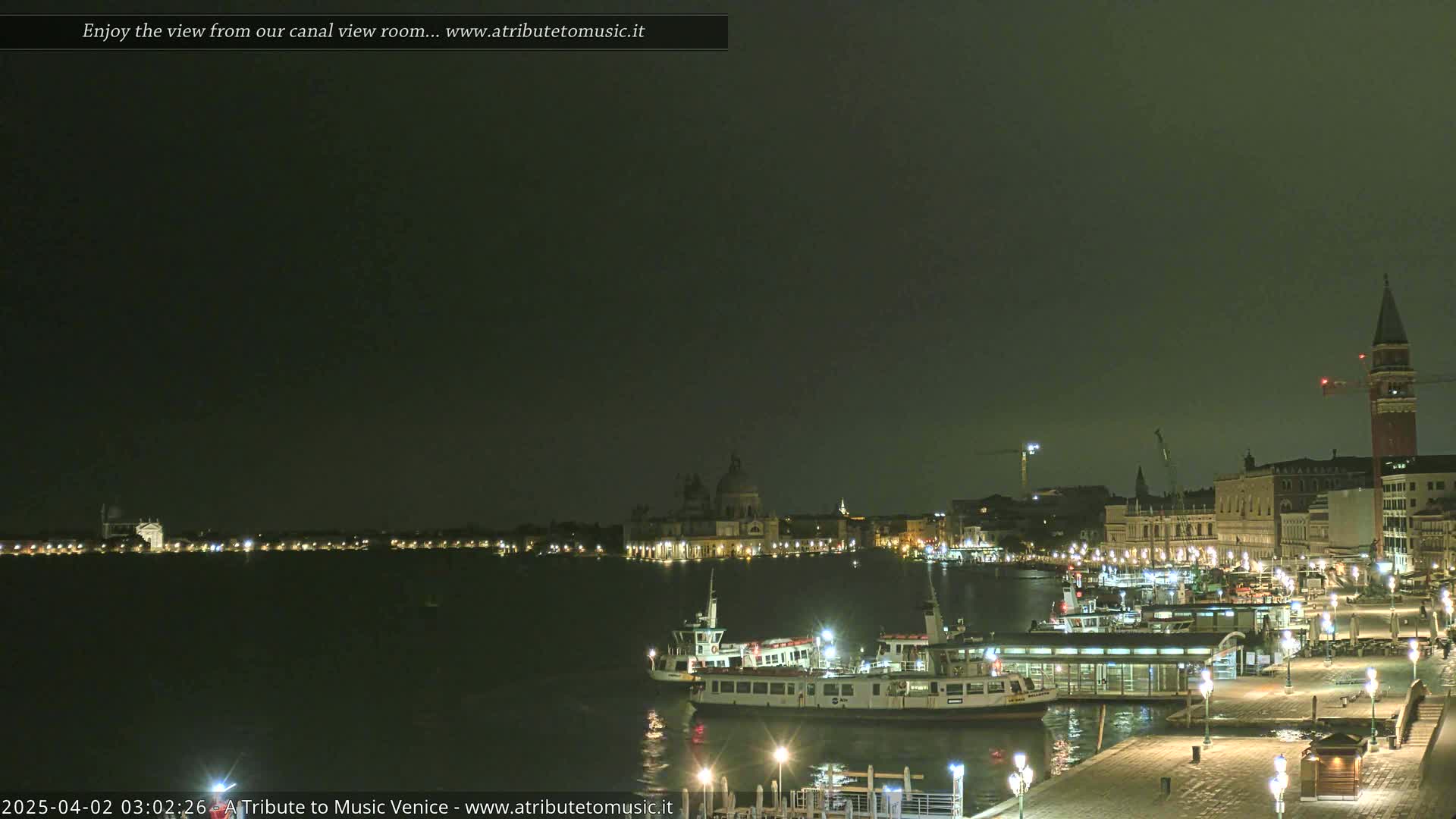 Nighttime view of a canal in Venice, Italy, with illuminated buildings, boats, and a dark, overcast sky.