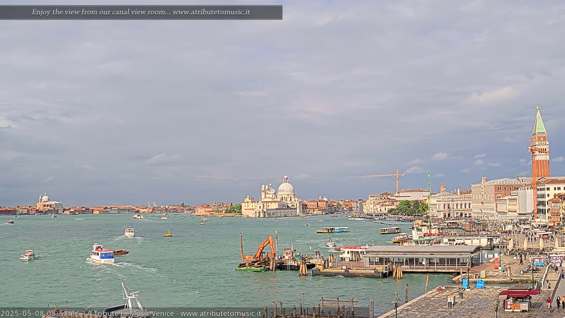 A wide shot of a Venetian canal shows boats on the water, buildings lining the shore, and a cloudy sky overhead.