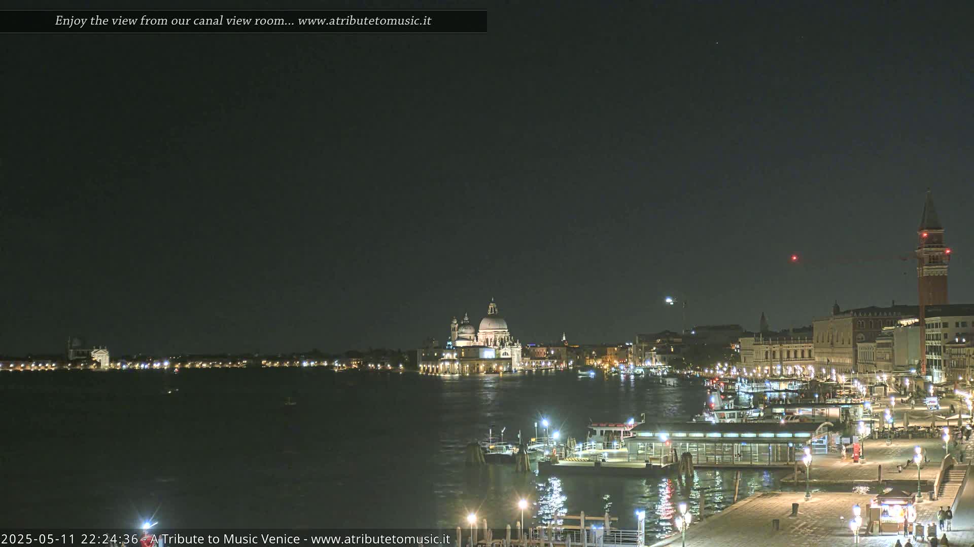 A nighttime view of a canal in Venice, with illuminated buildings and boats, under a clear, dark sky.