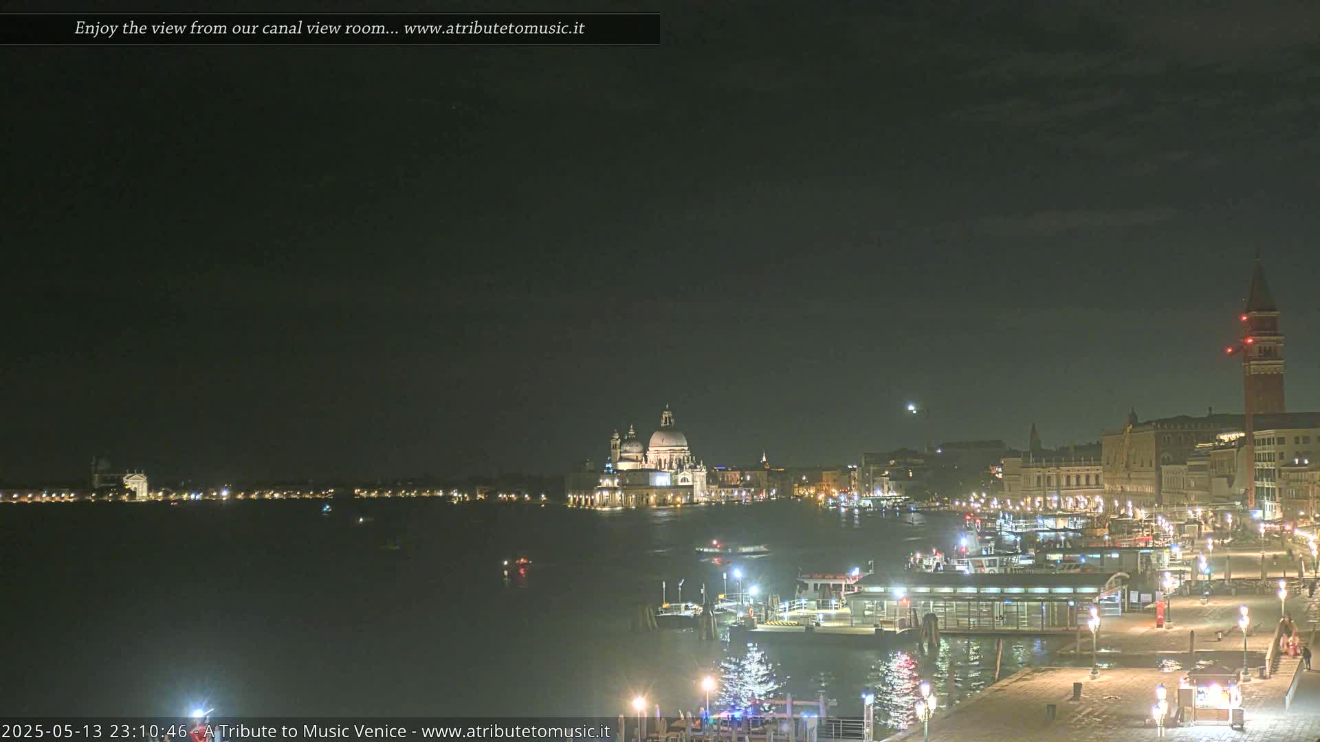 A nighttime view of a canal in Venice, with illuminated buildings and boats, under a dark, mostly clear sky.