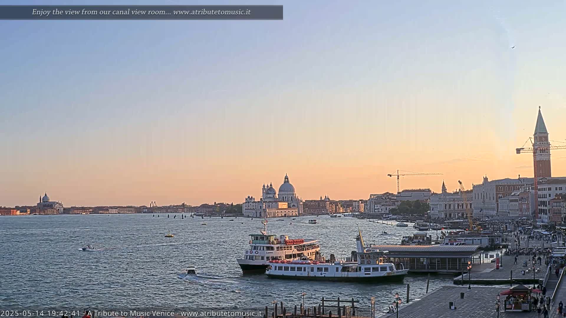A calm sunset illuminates a Venetian canal scene with several boats near a waterfront, showcasing the Basilica di Santa Maria della Salute and the Campanile di San Marco in the distance.