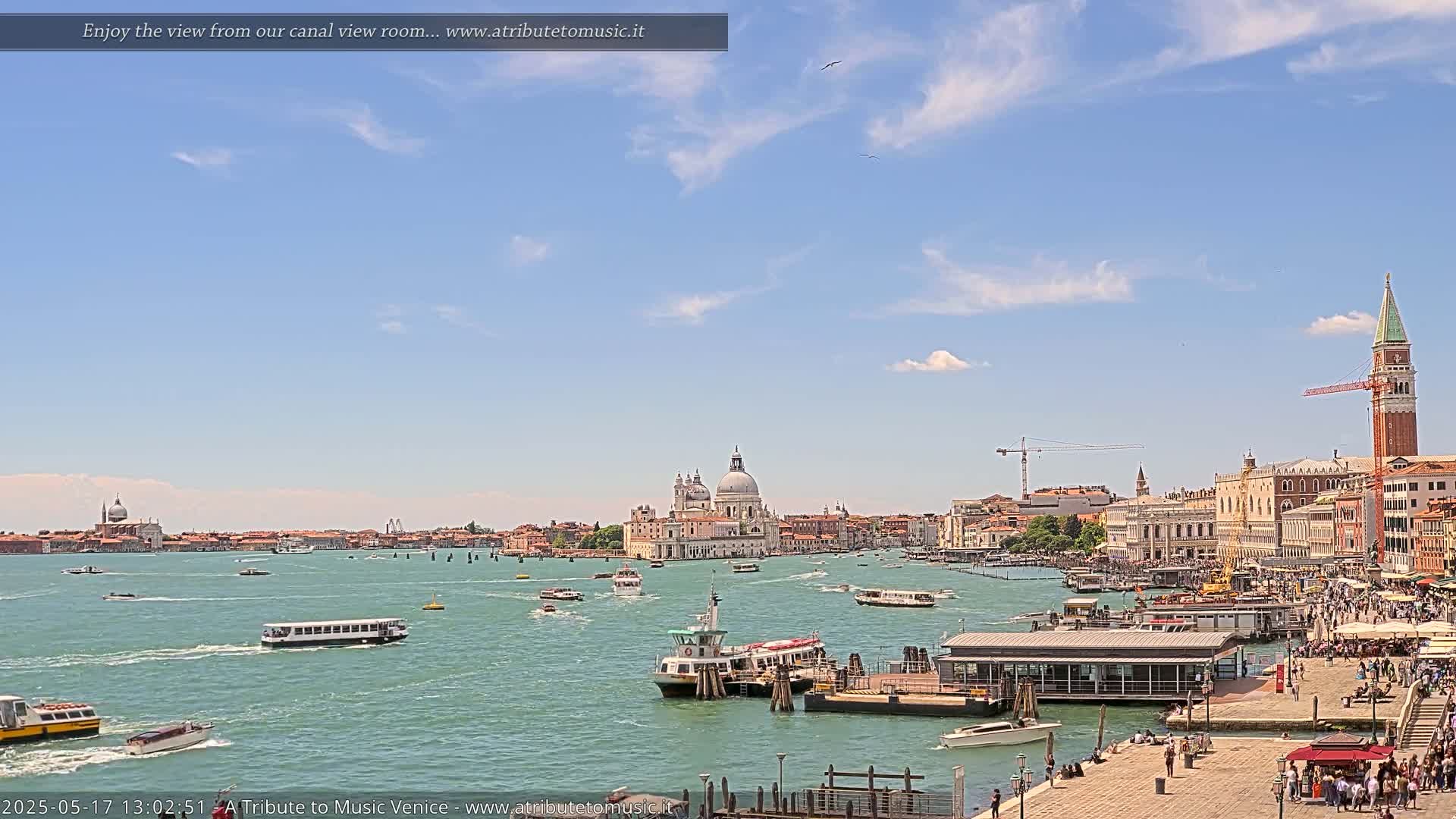 A sunny Venetian cityscape with numerous boats on the water, featuring the Basilica di Santa Maria della Salute and the St. Mark's Campanile in the distance.