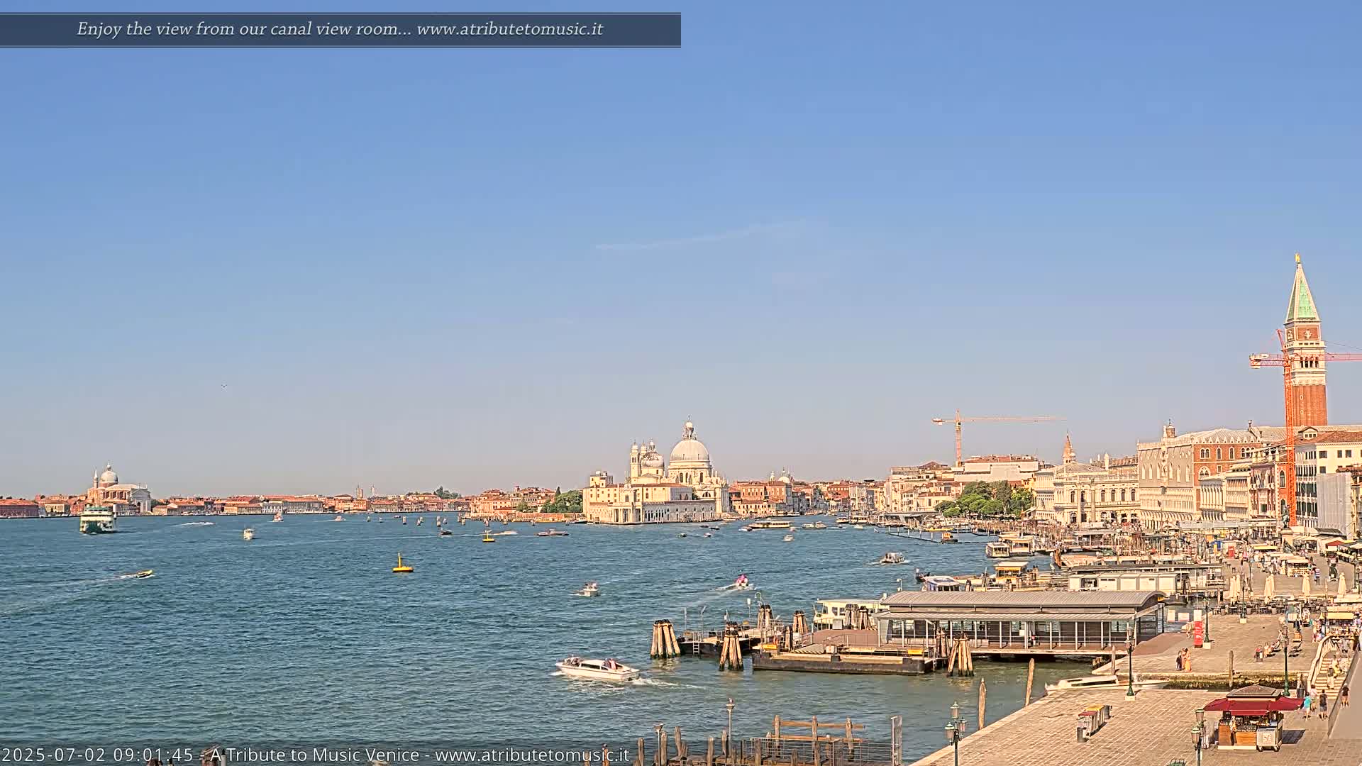 A sunny day in Venice shows a wide canal with boats, a waterfront with buildings, and a church in the distance.
