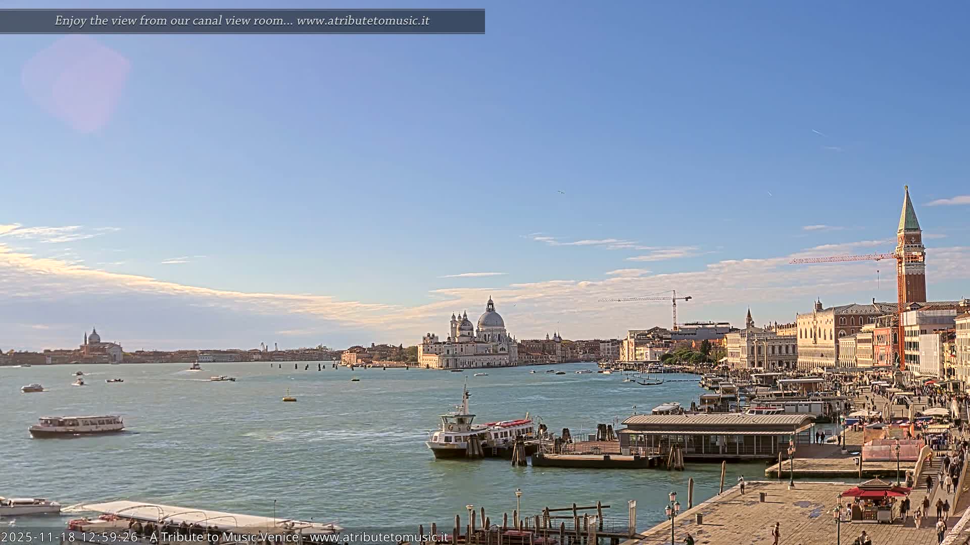 The image displays a clear night scene of a calm body of water with boats docked along a waterfront, illuminated by numerous city lights reflecting on the surface, under a dark, clear sky.