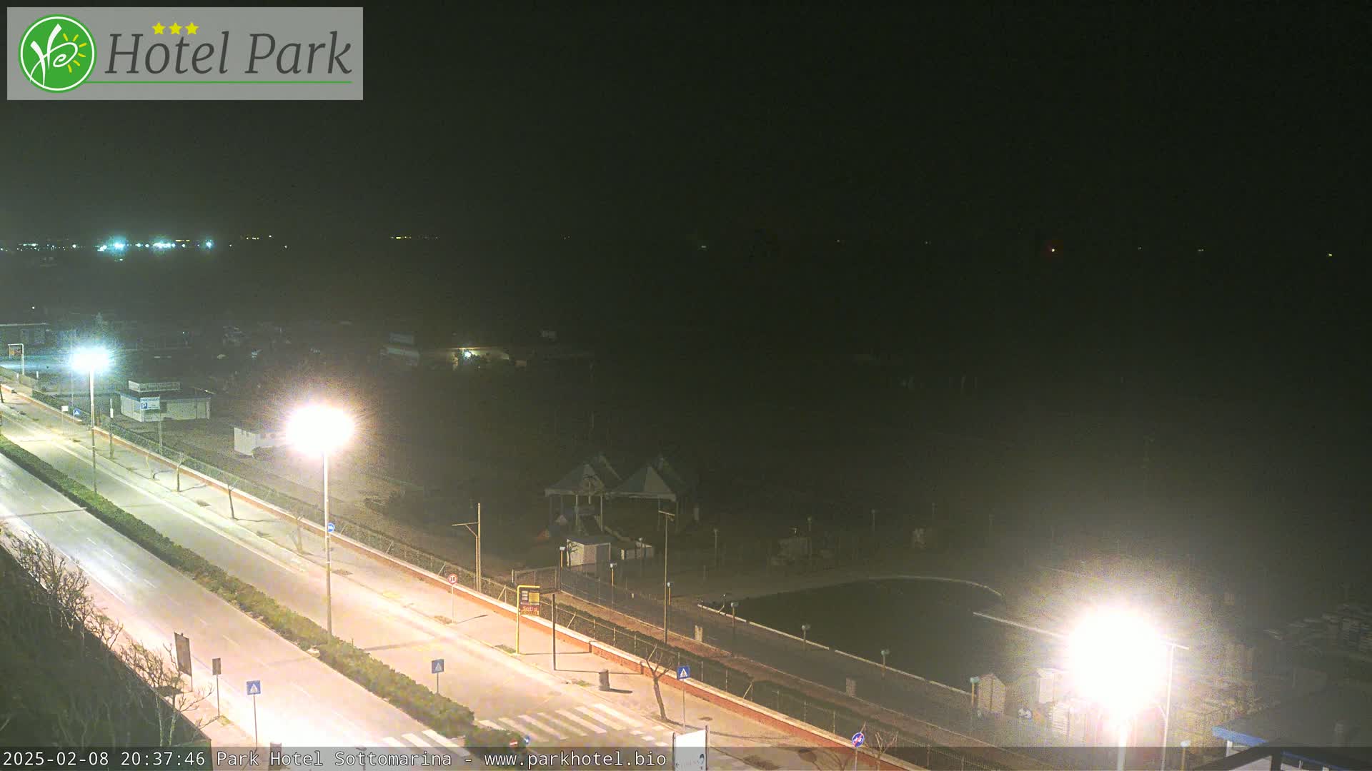 A nighttime long shot of a road and beachfront area with a few lights illuminating the scene.