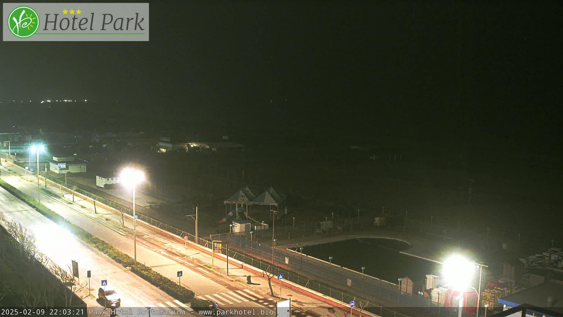 A nighttime view of a road, a playground, a pool, and other buildings under a dark sky.