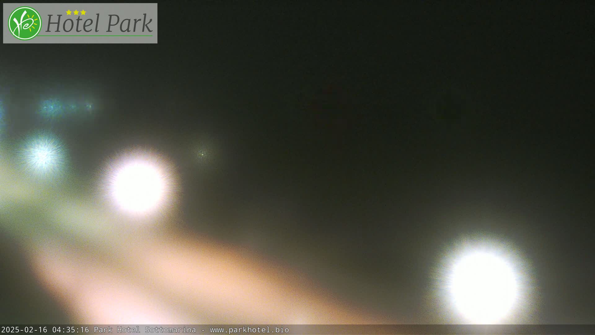 A hazy, dark nighttime scene shows several bright lights, likely from vehicle headlights, in the distance.