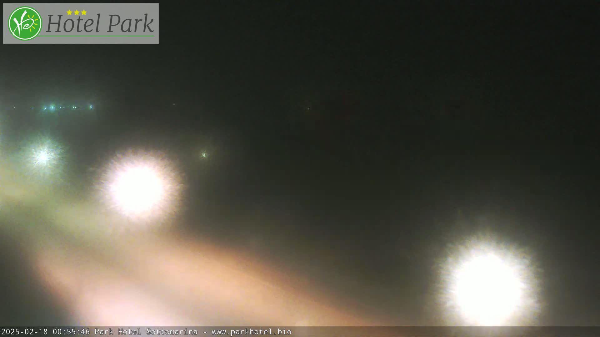 A foggy night scene shows the bright headlights of vehicles on a road.