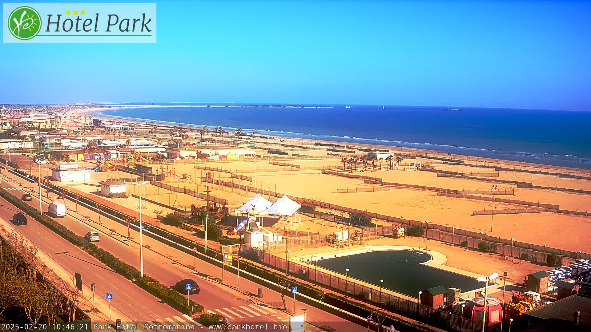 A beach with volleyball courts, a swimming pool, and playground equipment is visible from a high vantage point on a sunny day.