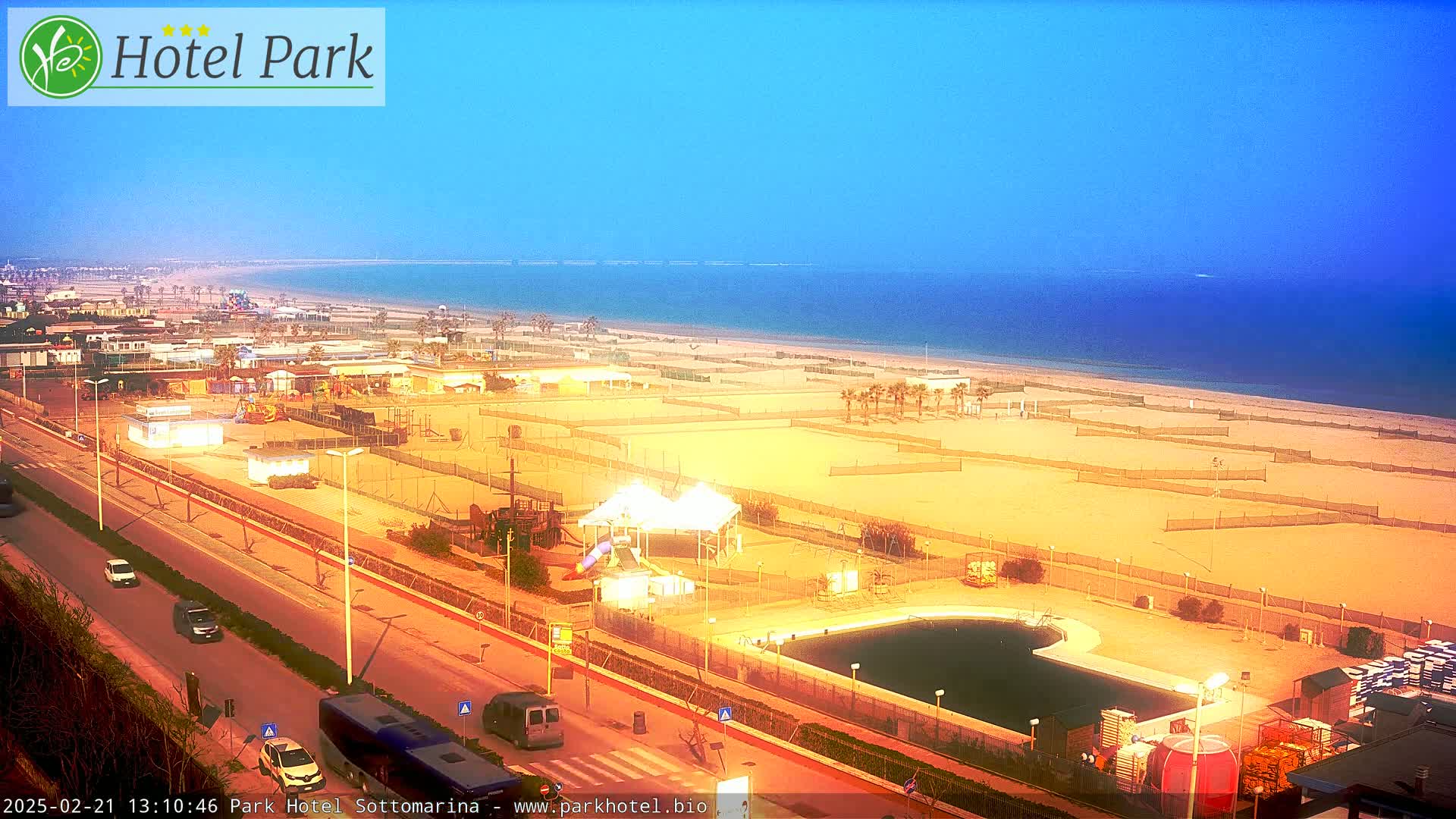 A beachside resort area with a pool, playground, and volleyball courts is visible under a clear, twilight sky.