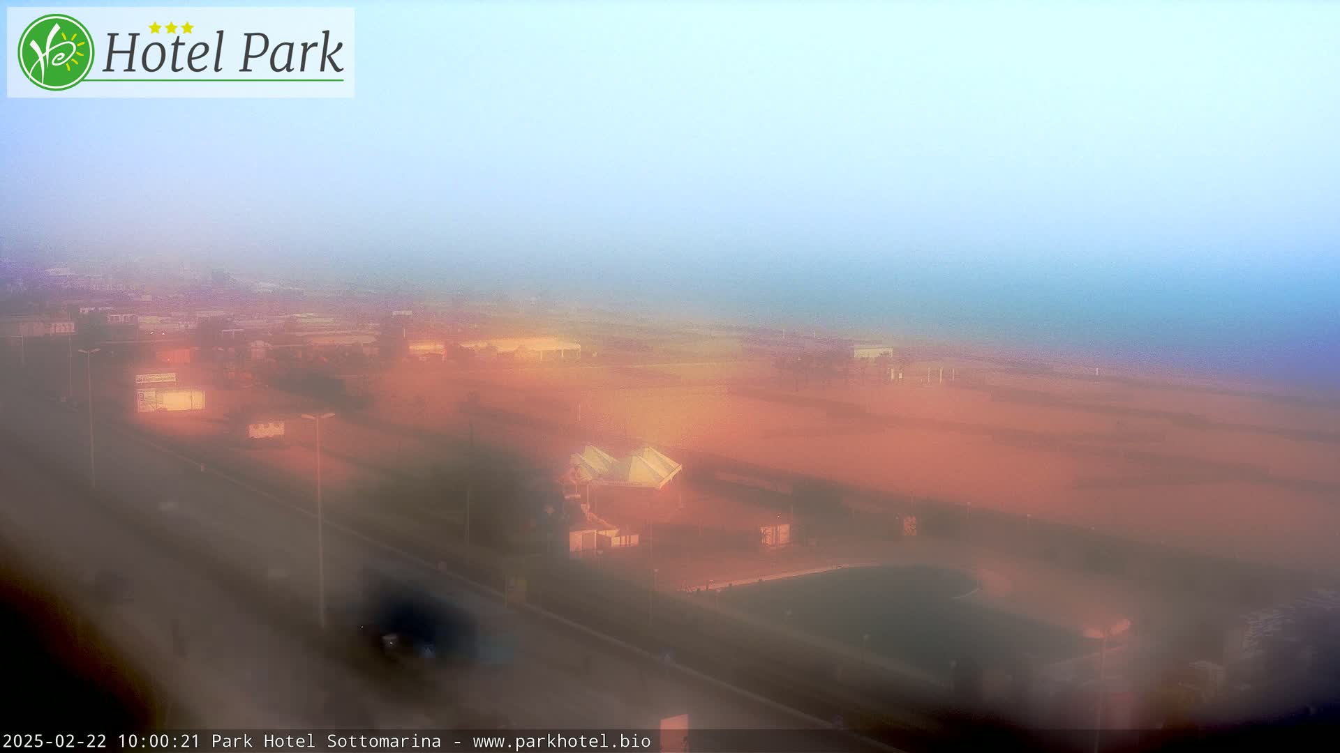 A hazy, orange-tinged coastal scene is visible from a high vantage point, showing a road, buildings, and a beach shrouded in fog.
