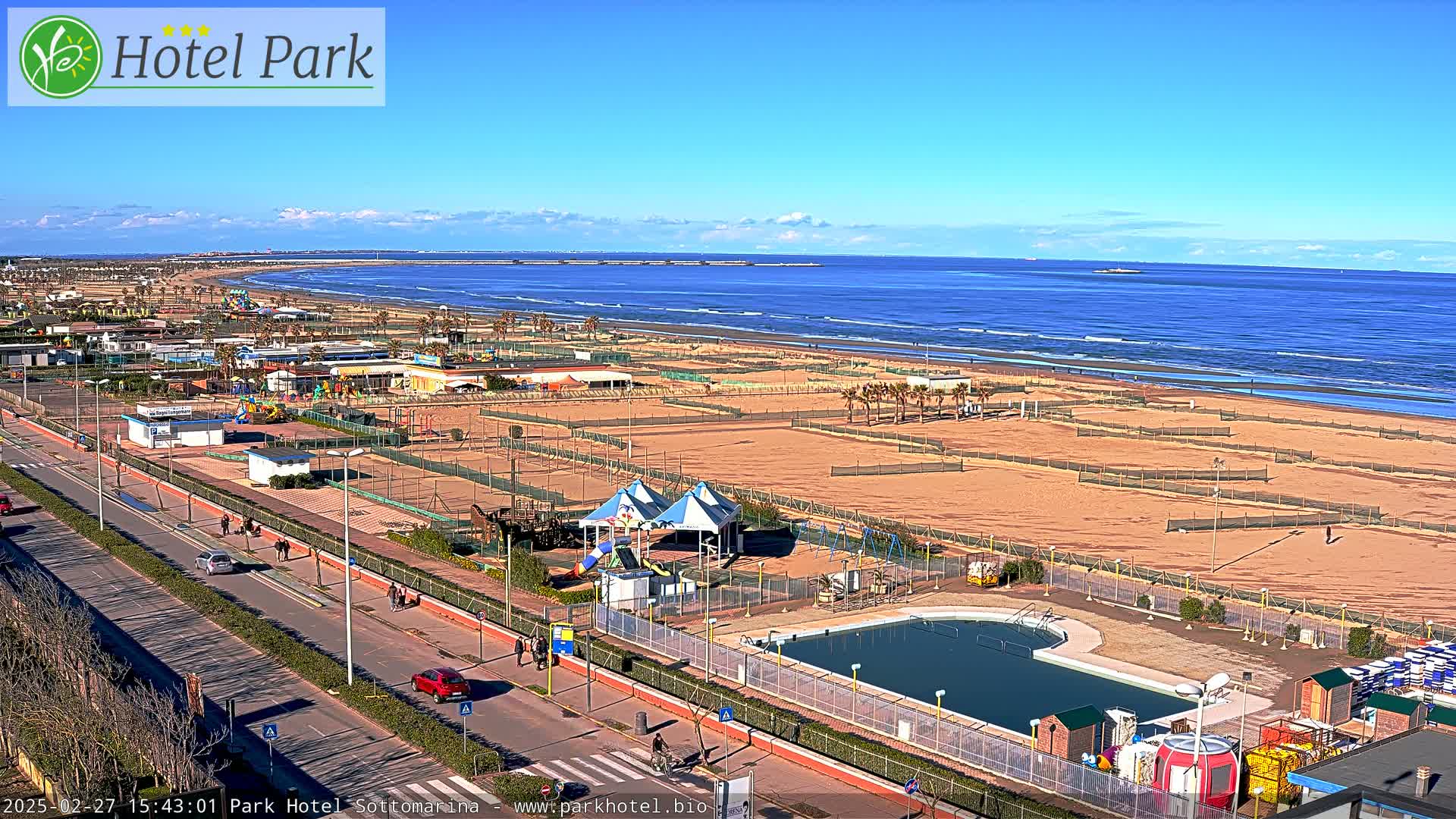 A beachside resort area with a swimming pool and playground is shown on a sunny day with a calm ocean in the background.
