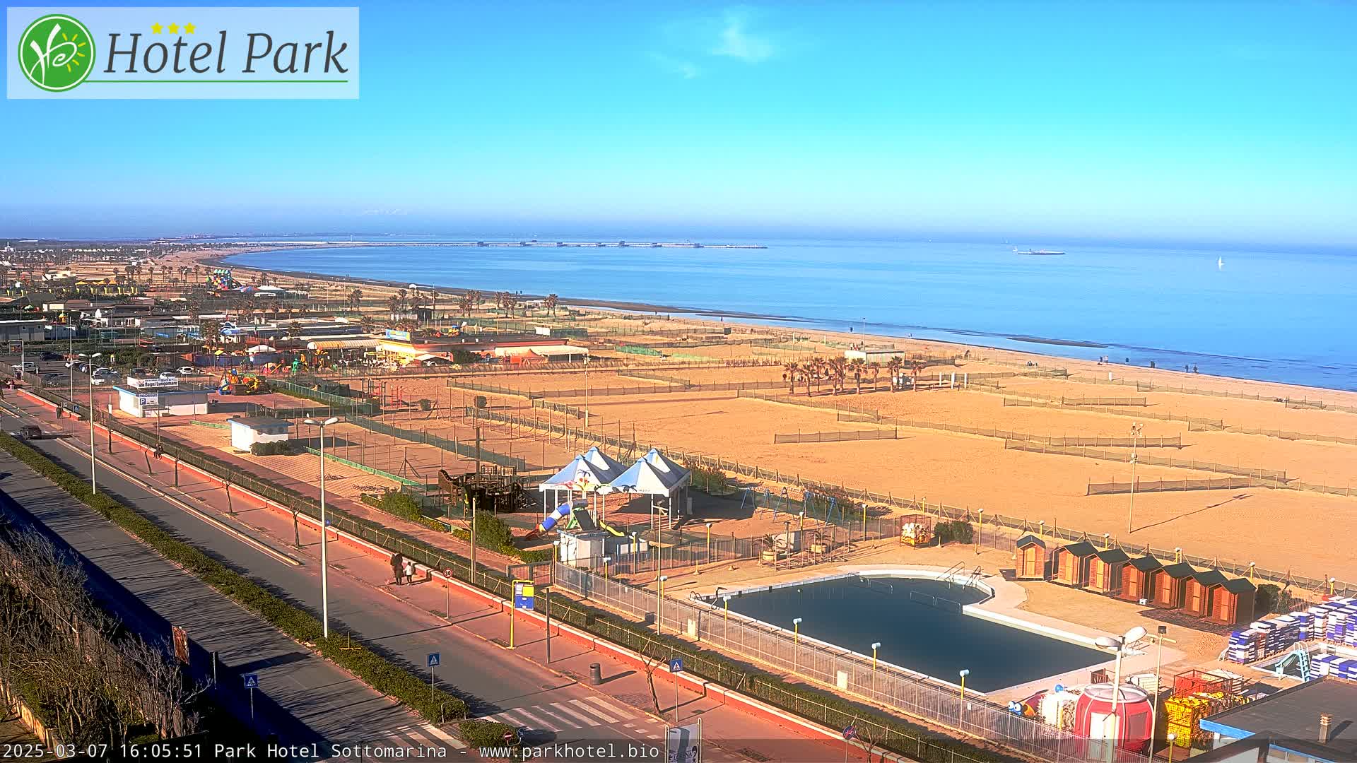 A beachside amusement park with a swimming pool is seen on a sunny day, next to a calm ocean.