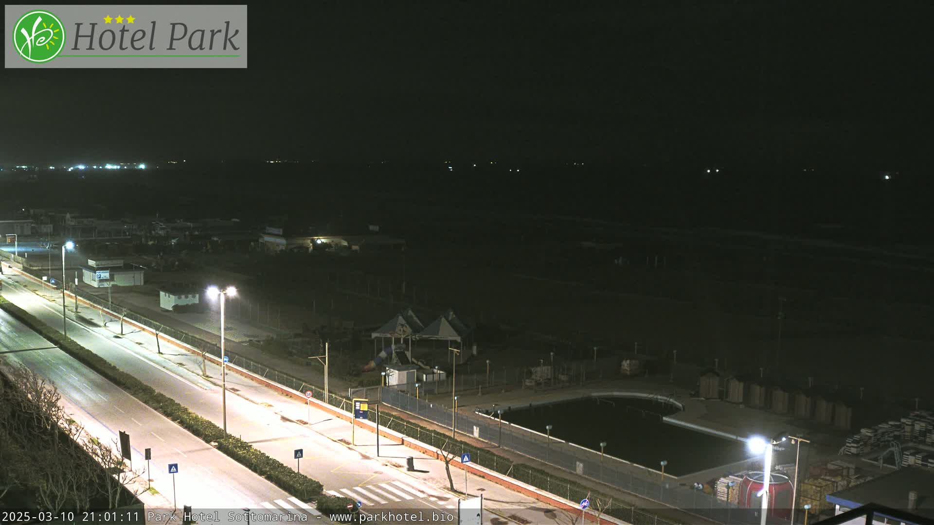A nighttime aerial view shows a mostly empty road next to a closed swimming pool and playground area.