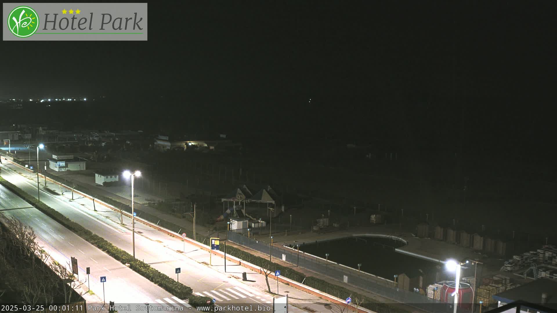 A nighttime view of a mostly empty road next to a closed-down water park and swimming pool area.