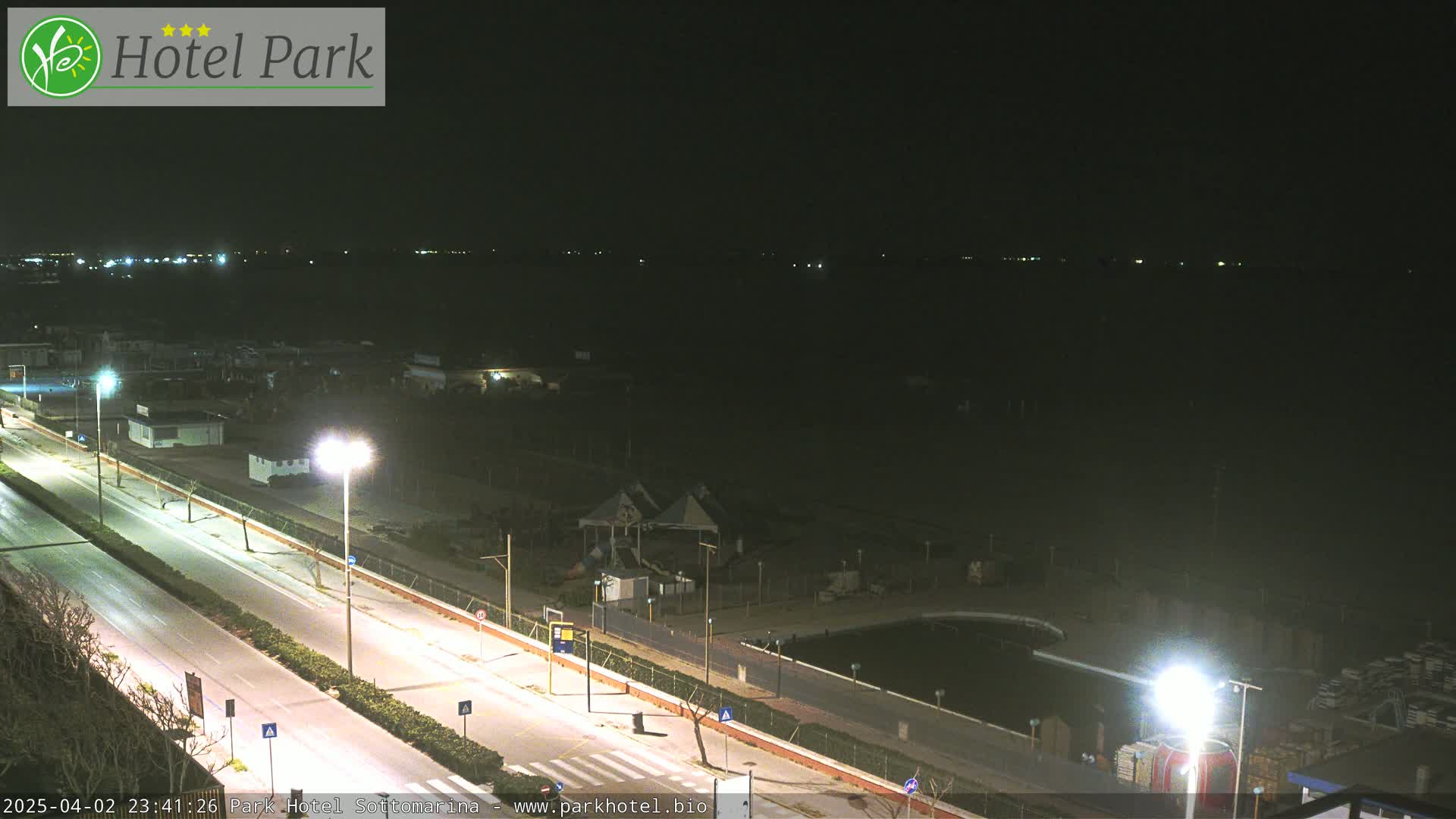 A nighttime view of a coastal road and beach area, with streetlights illuminating the scene.